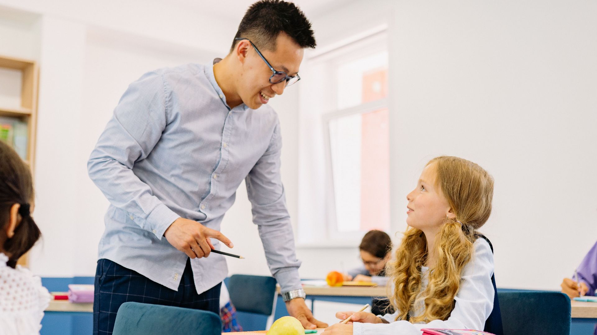 A male teacher interacting with diverse students in a bright classroom setting, promoting active learning.