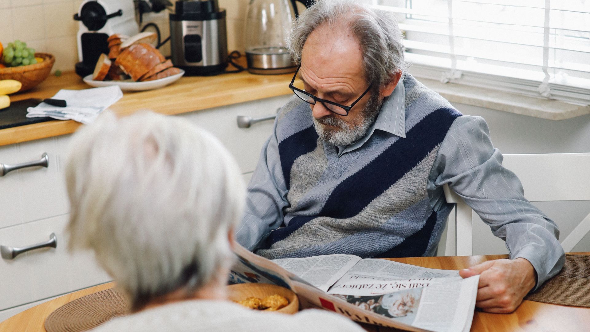 Senior couple enjoying a quiet morning in their kitchen, reading a newspaper together.