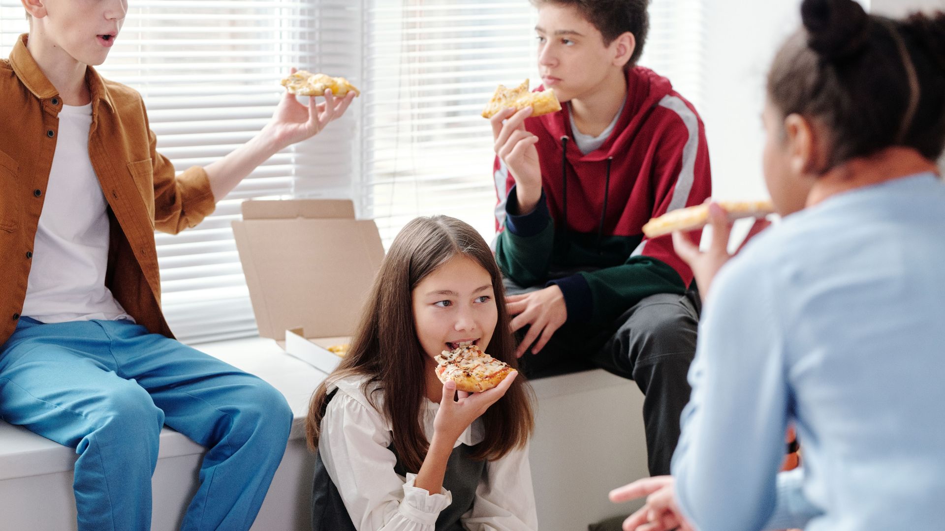 Group of teenagers having fun, enjoying pizza together indoors.
