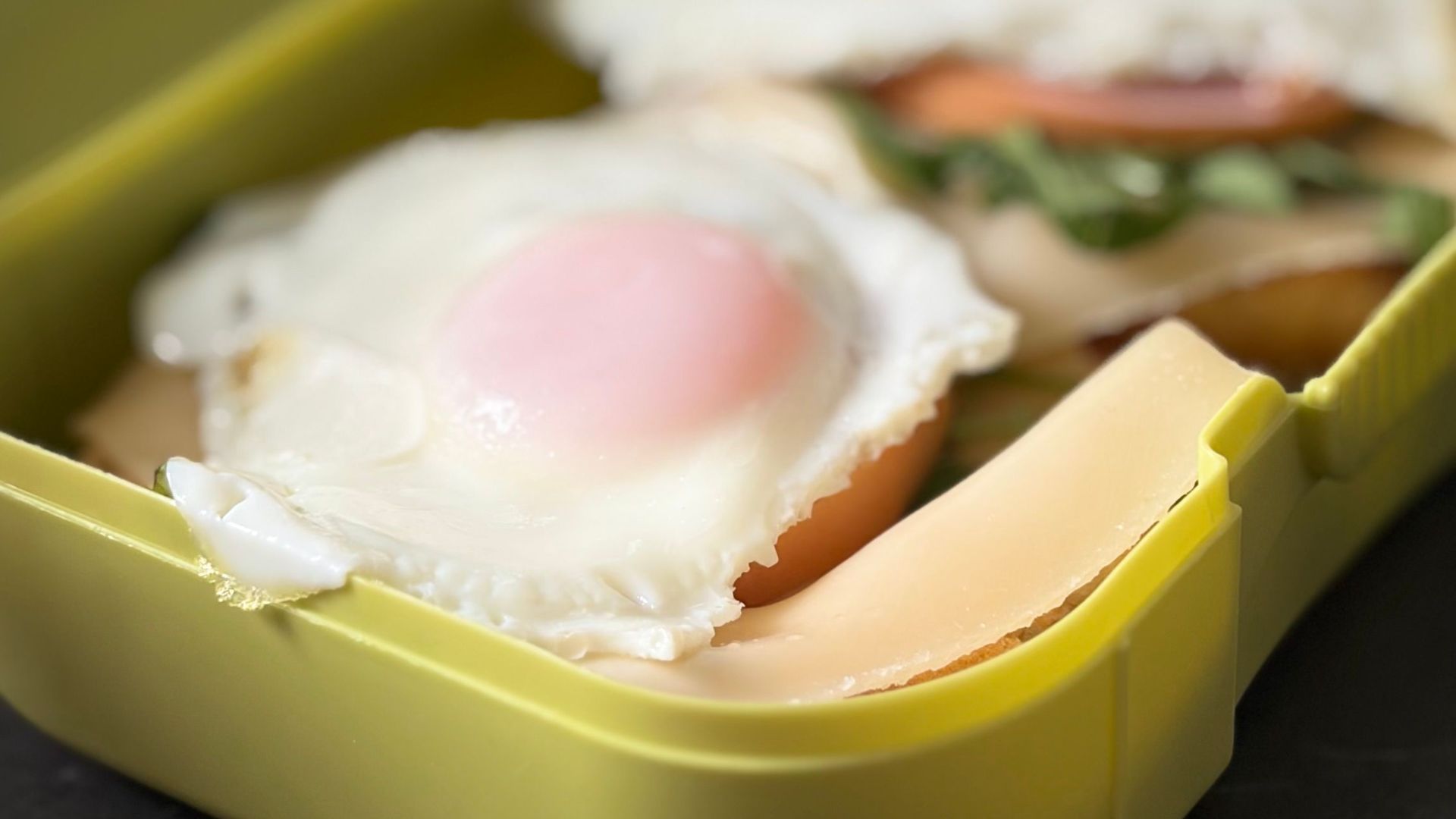Delicious breakfast sandwiches with eggs in a bright yellow lunch box on a table.