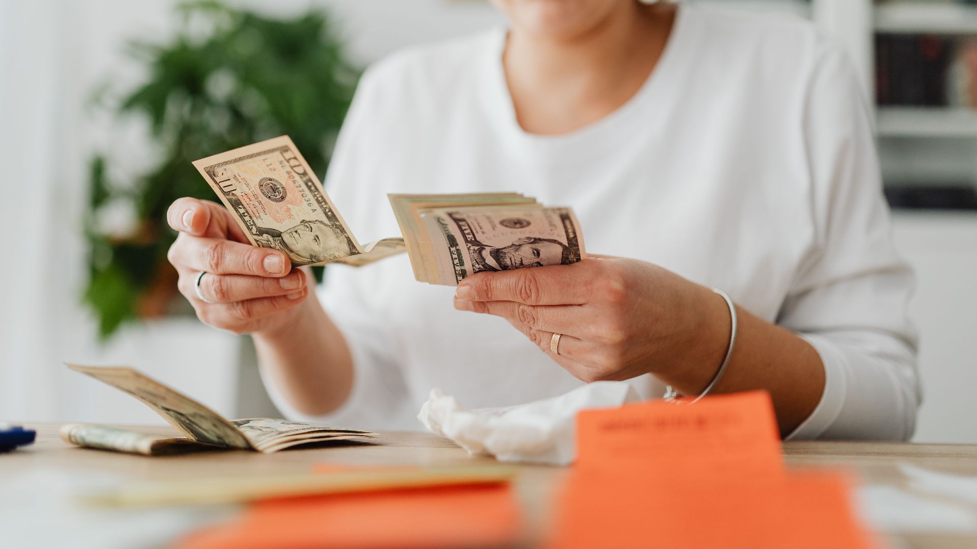 A woman sits indoors counting cash at her office desk, focusing on finances.