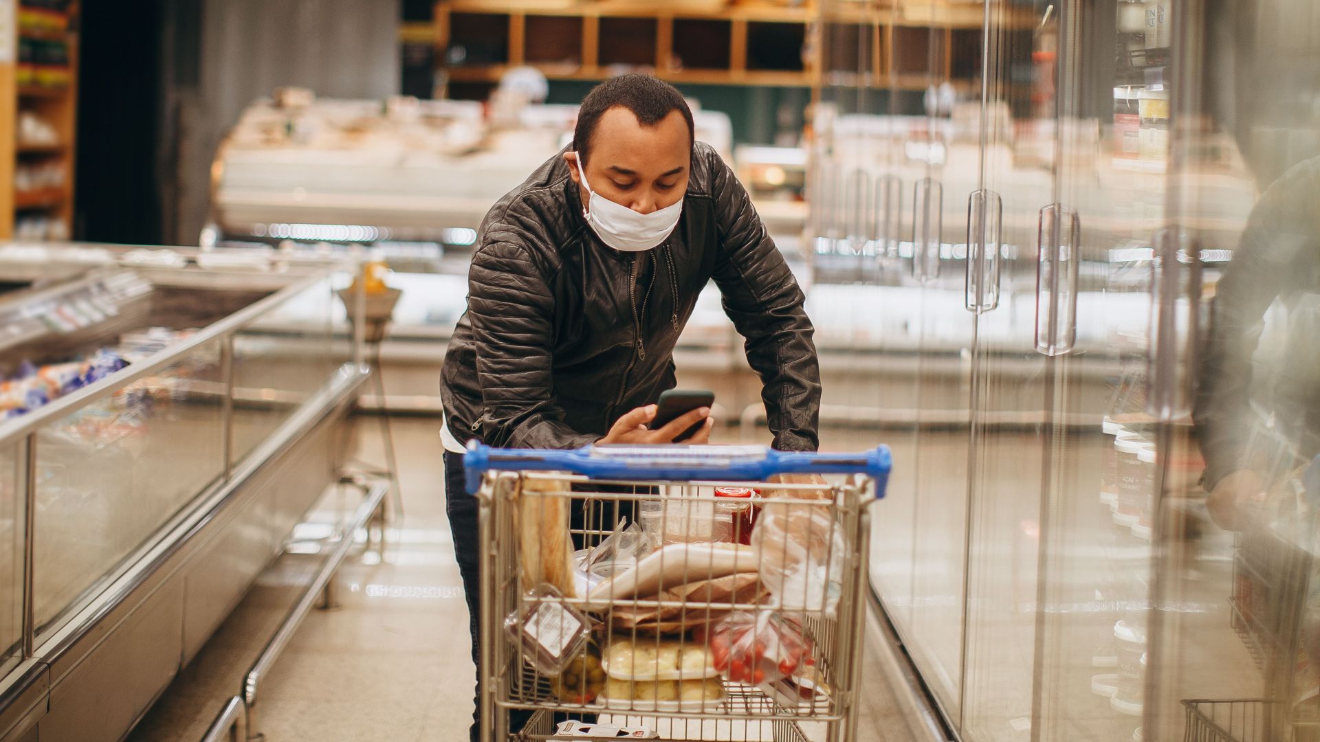 Man wearing mask shops in a supermarket, pushing a cart in the aisle.