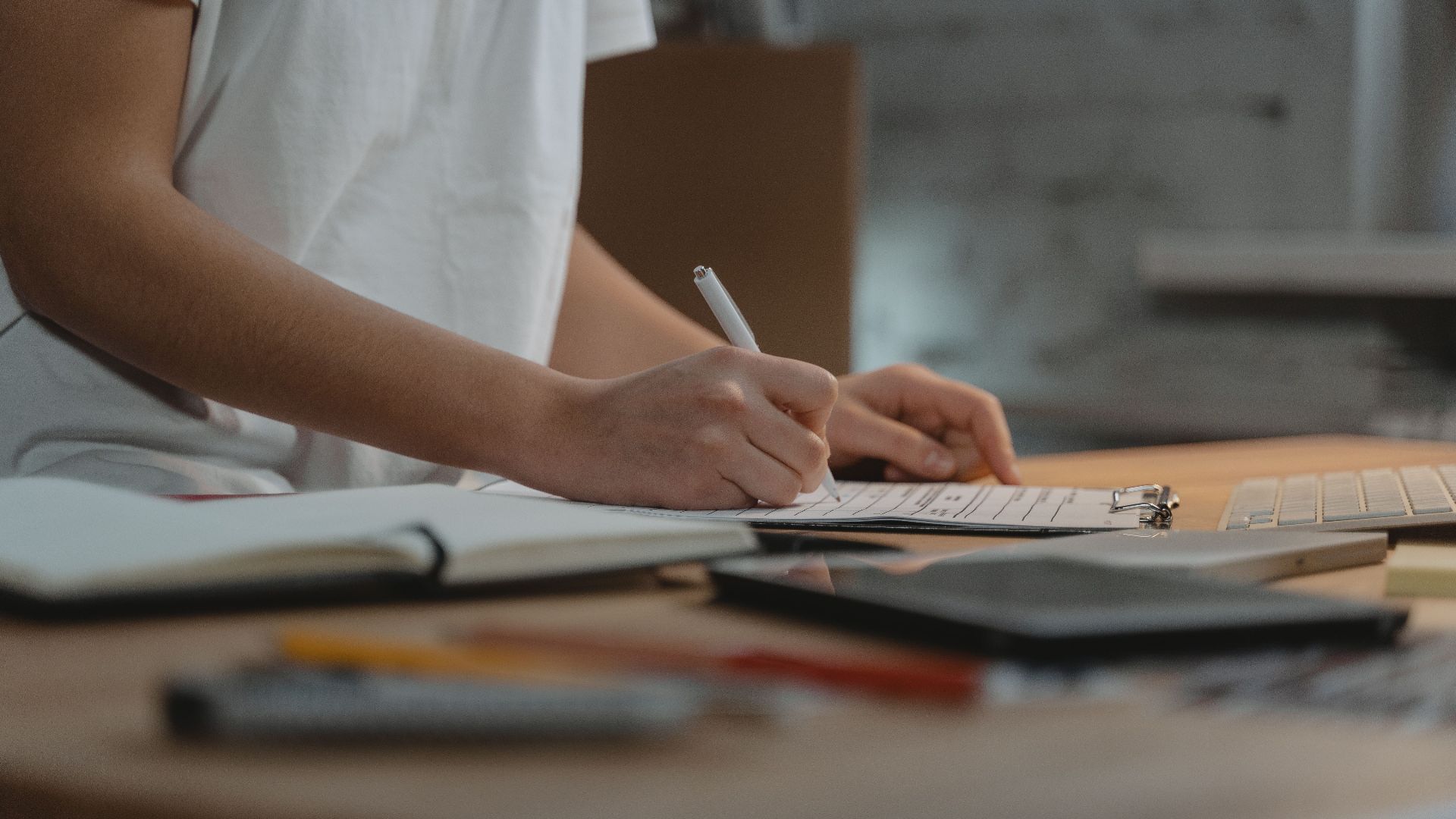 Close-up of individual writing on a clipboard at a desk with office supplies.
