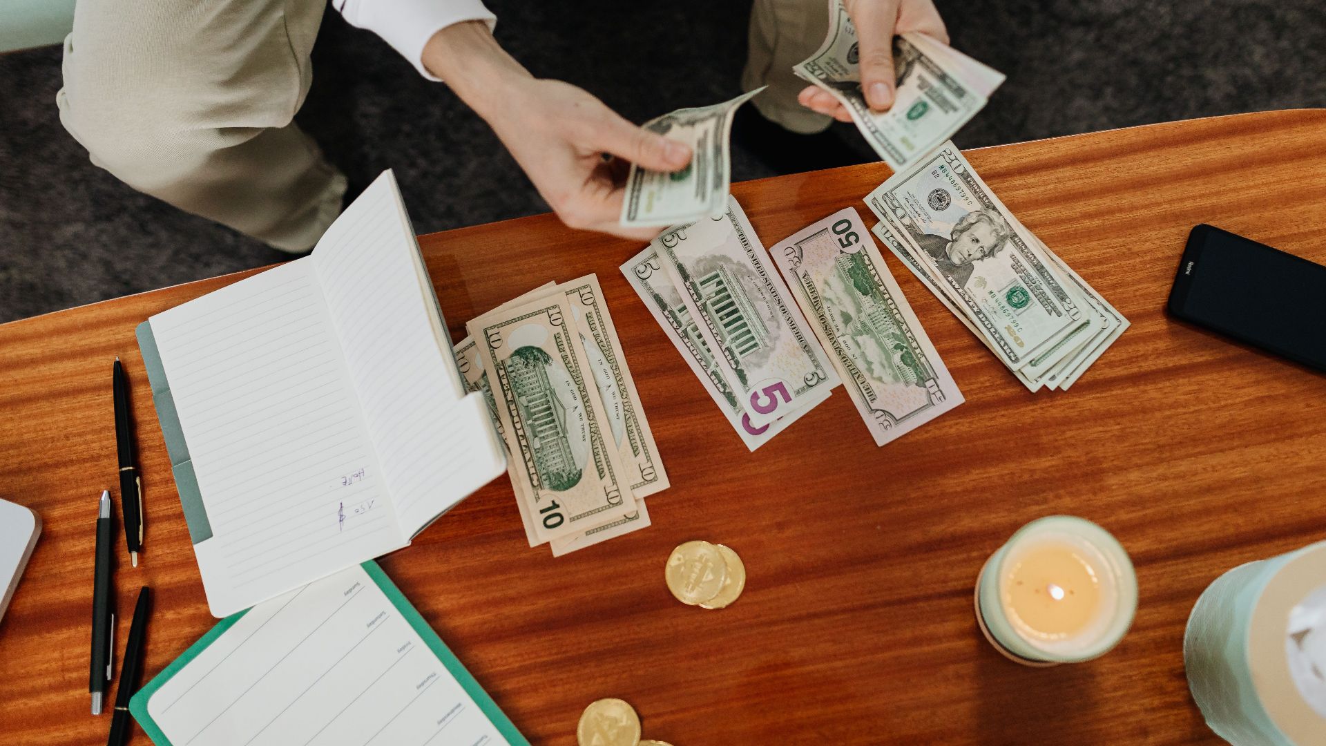 A person sitting and counting various US dollar bills at a table indoors.