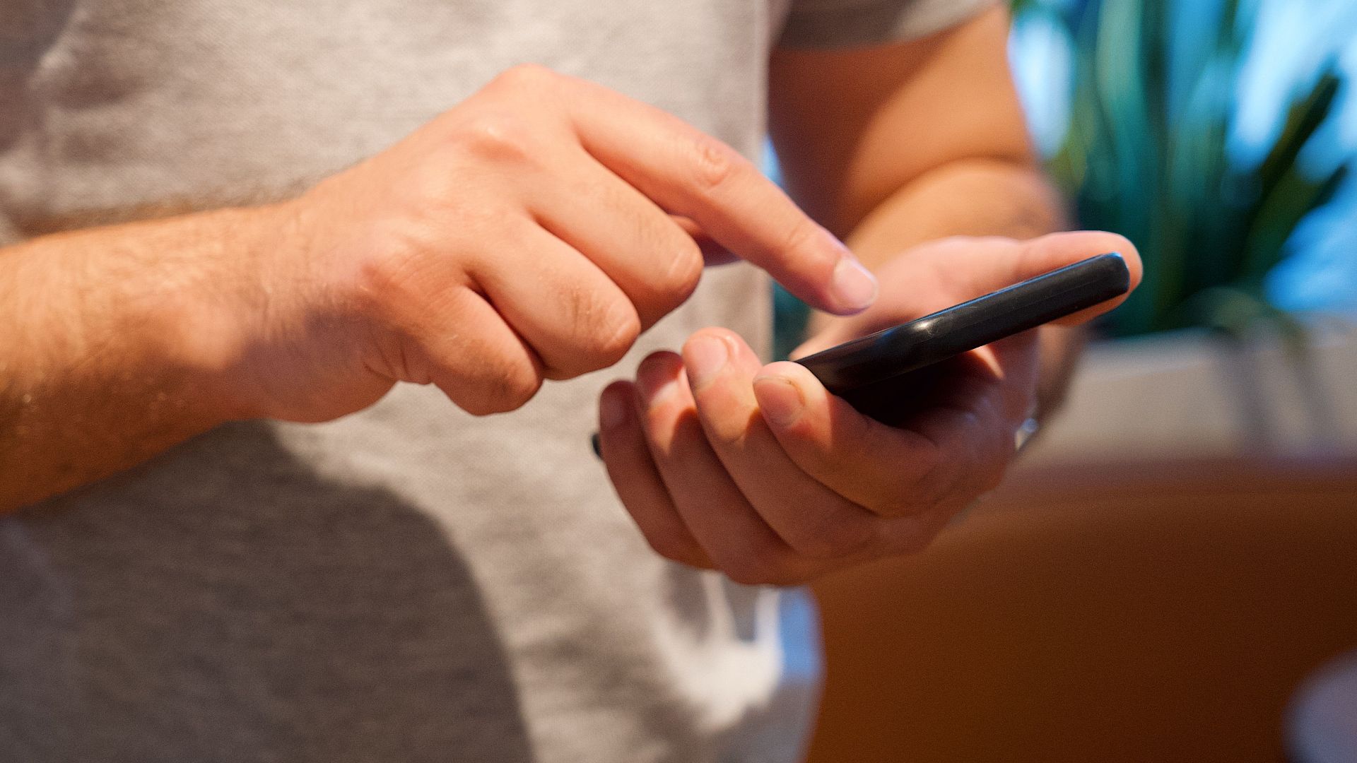 Adult male using smartphone in a bright indoor setting, focusing on the device and interaction.