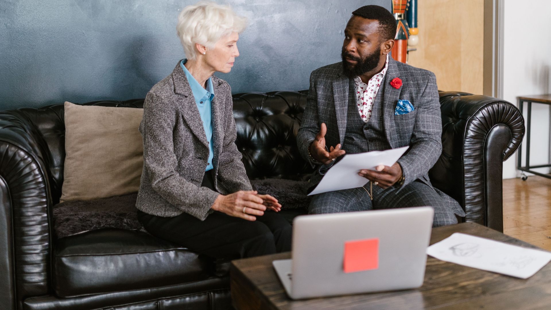 Two professionals engaged in a productive business discussion, seated on a leather couch in an office environment.
