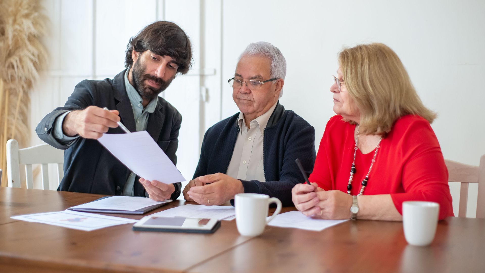 Elderly couple discussing documents with advisor at a wooden table indoors.