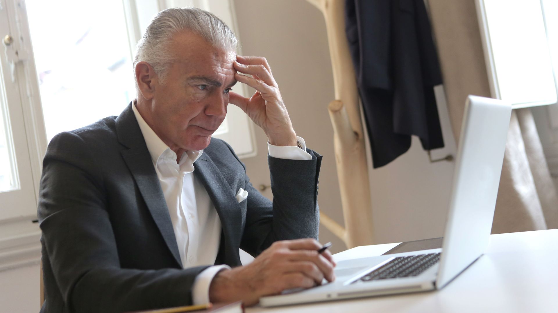 Senior businessman in office pondering work issues on laptop, showing stress.