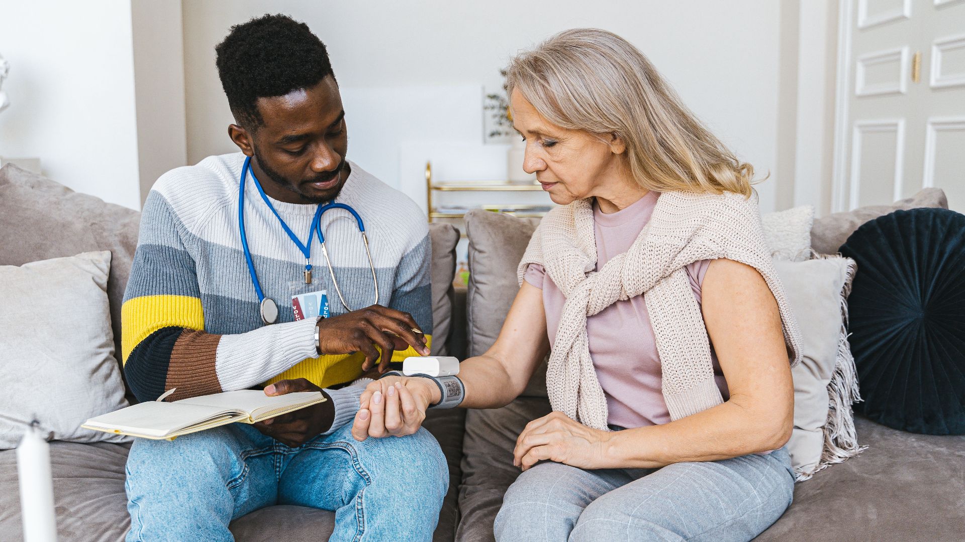Healthcare professional checking blood pressure of elderly woman in a cozy indoor setting.