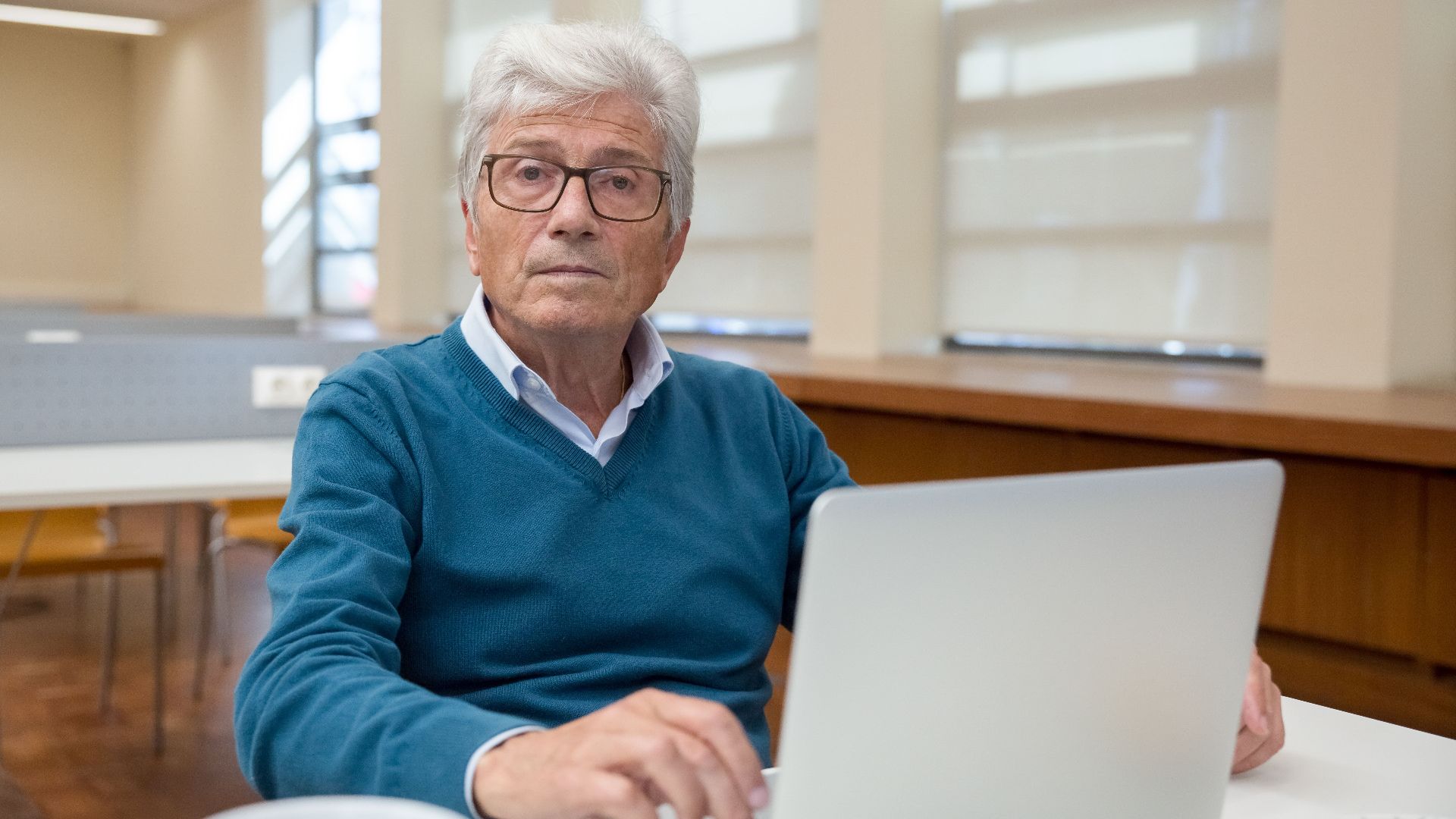 Senior man working remotely on a laptop in an office environment.