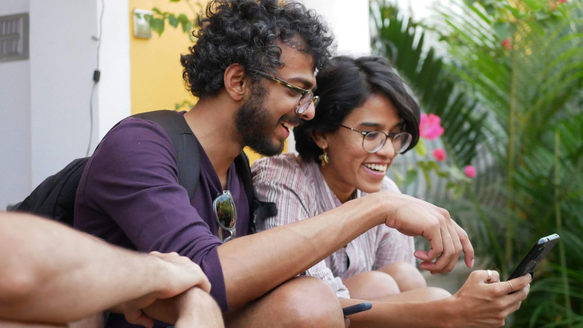 A man and a woman laughing while looking at a smartphone outdoors