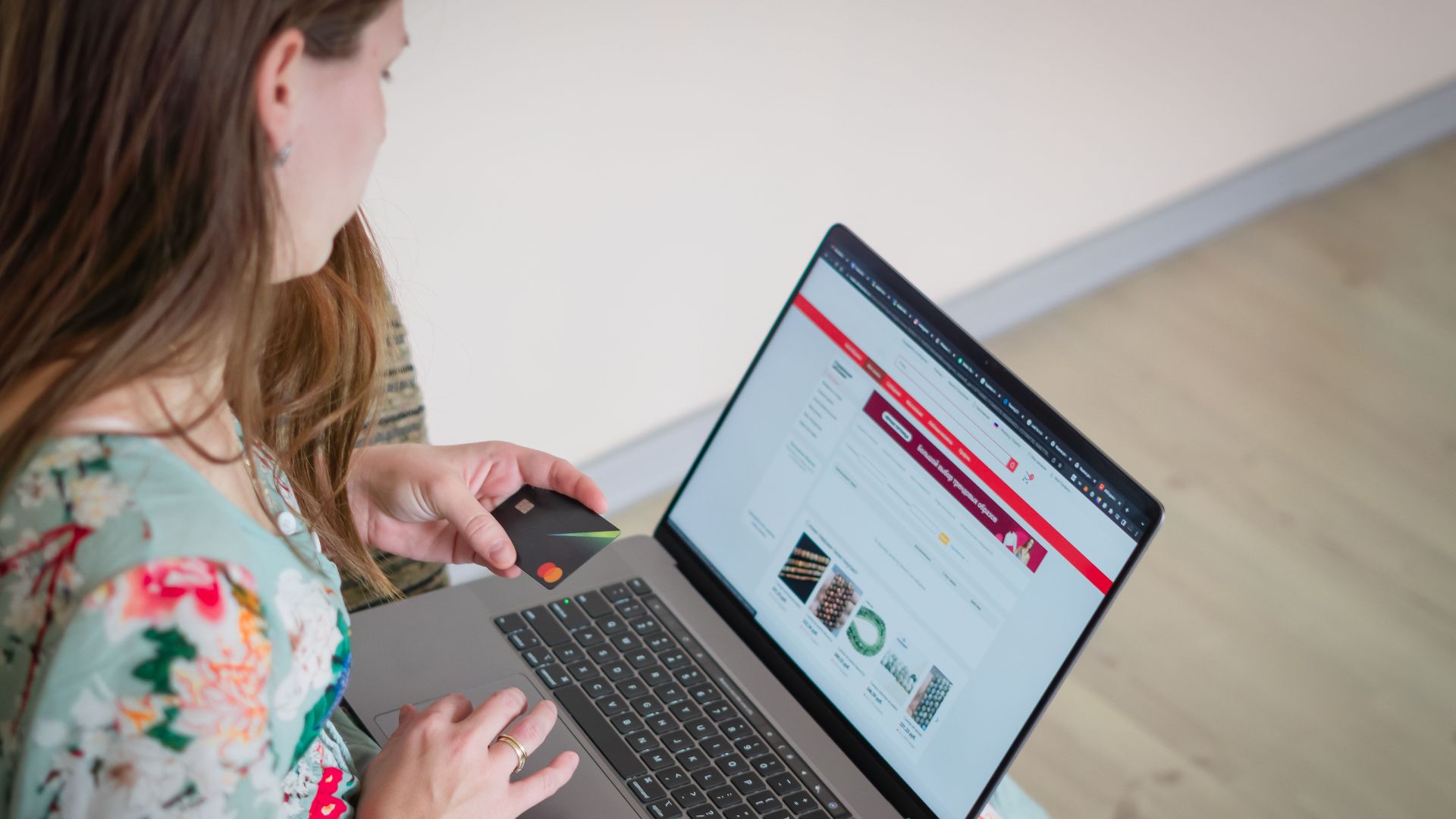 Woman in floral dress shopping online with a laptop and credit card indoors.