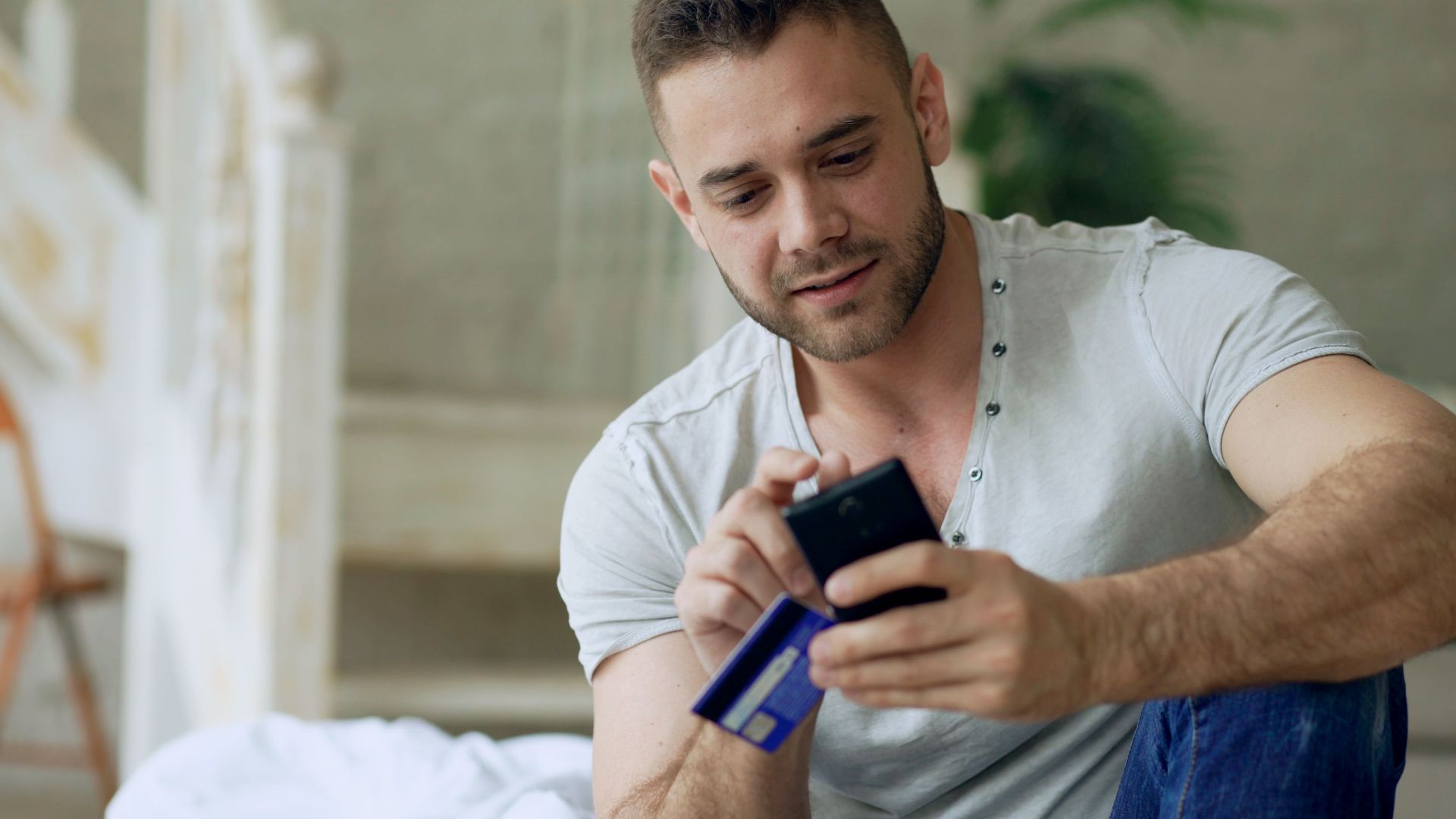 Young man using smartphone and credit card for online shopping indoors.