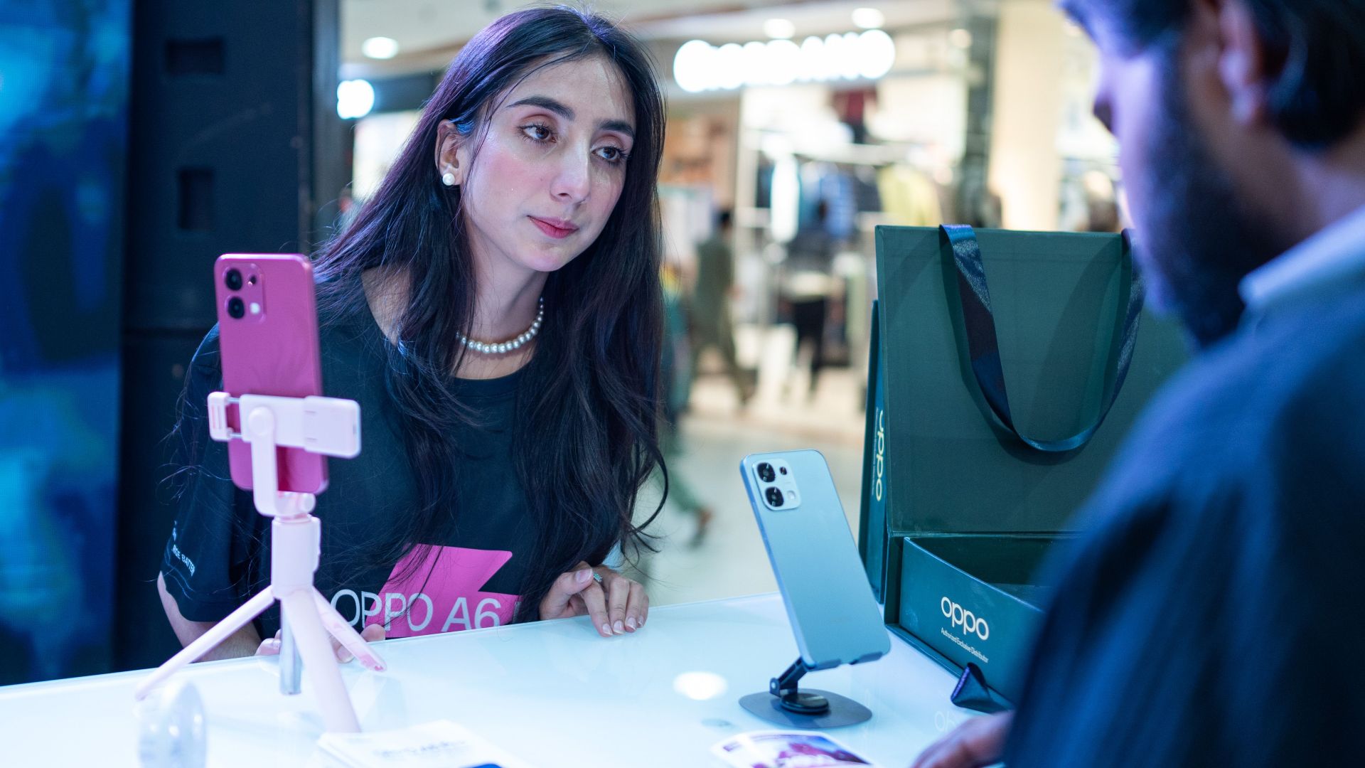 Woman at smartphone demo counter engages with salesperson in Islamabad retail setting.