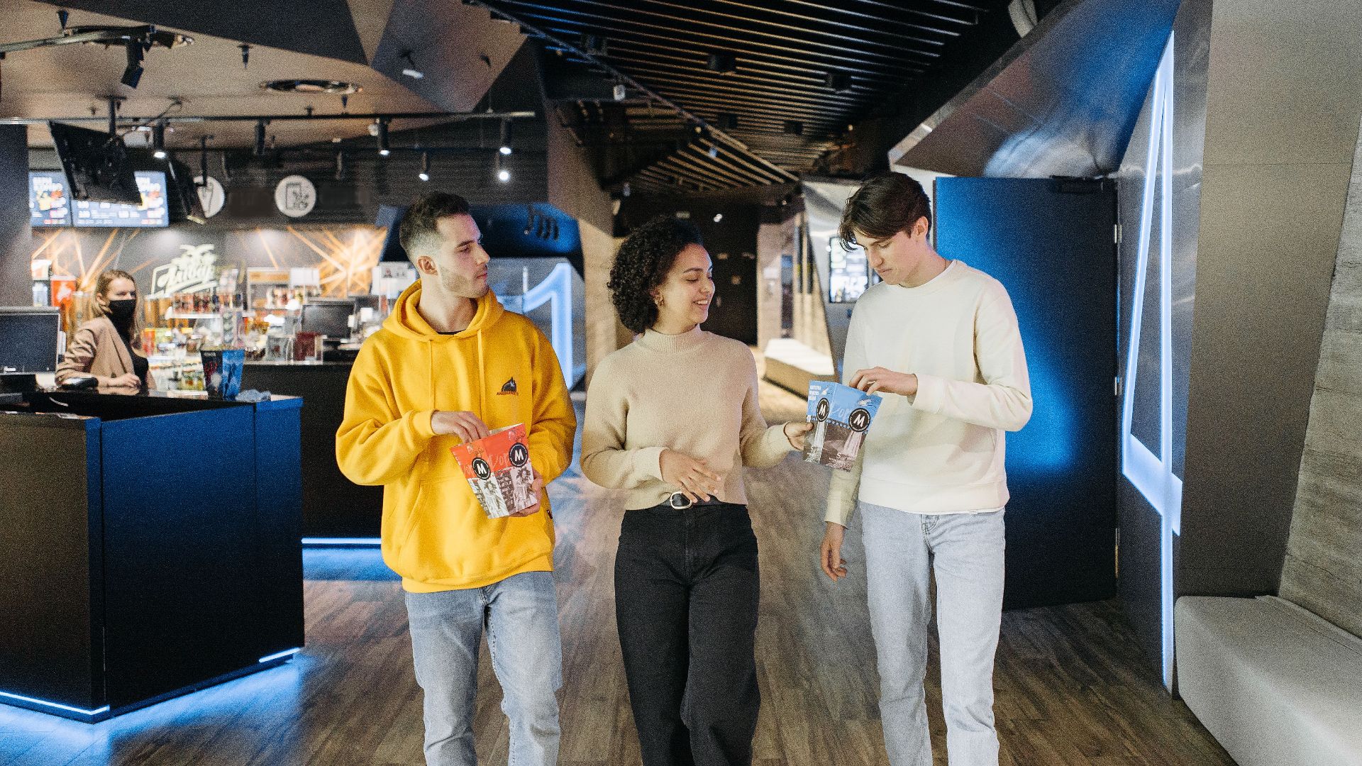 Three friends walking in a movie theater with popcorn, ready for a cinematic experience.