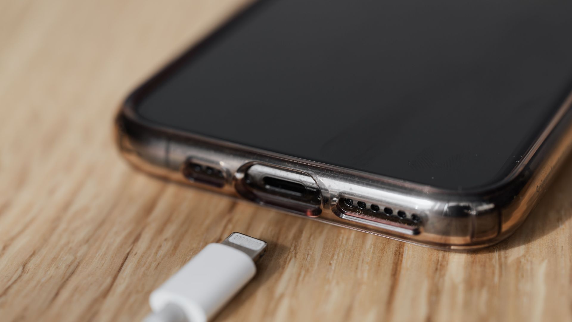 Modern cellphone in transparent cover with closeup of charging input and mobile phone white charger cable usb connector on wooden table