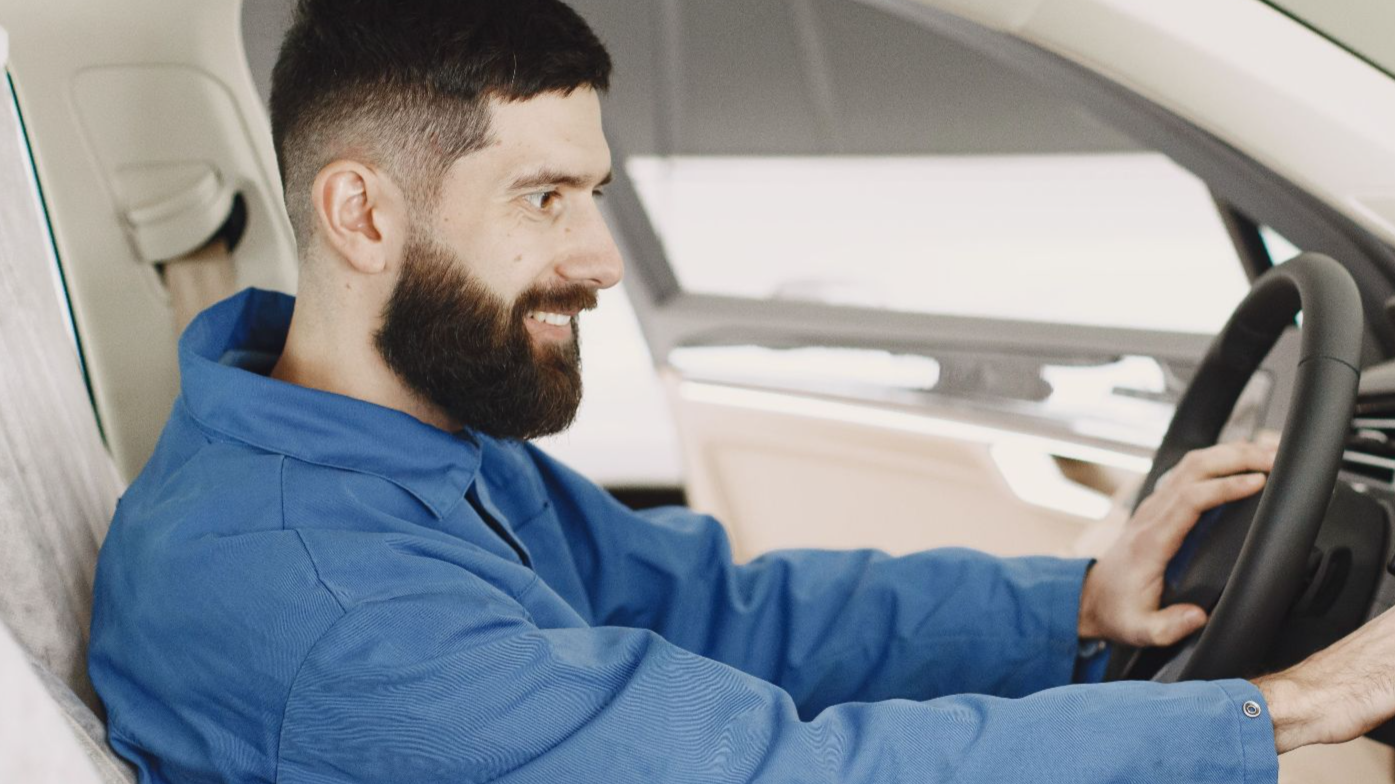 Mechanic in blue coveralls interacts with car dashboard, smiling and focused.