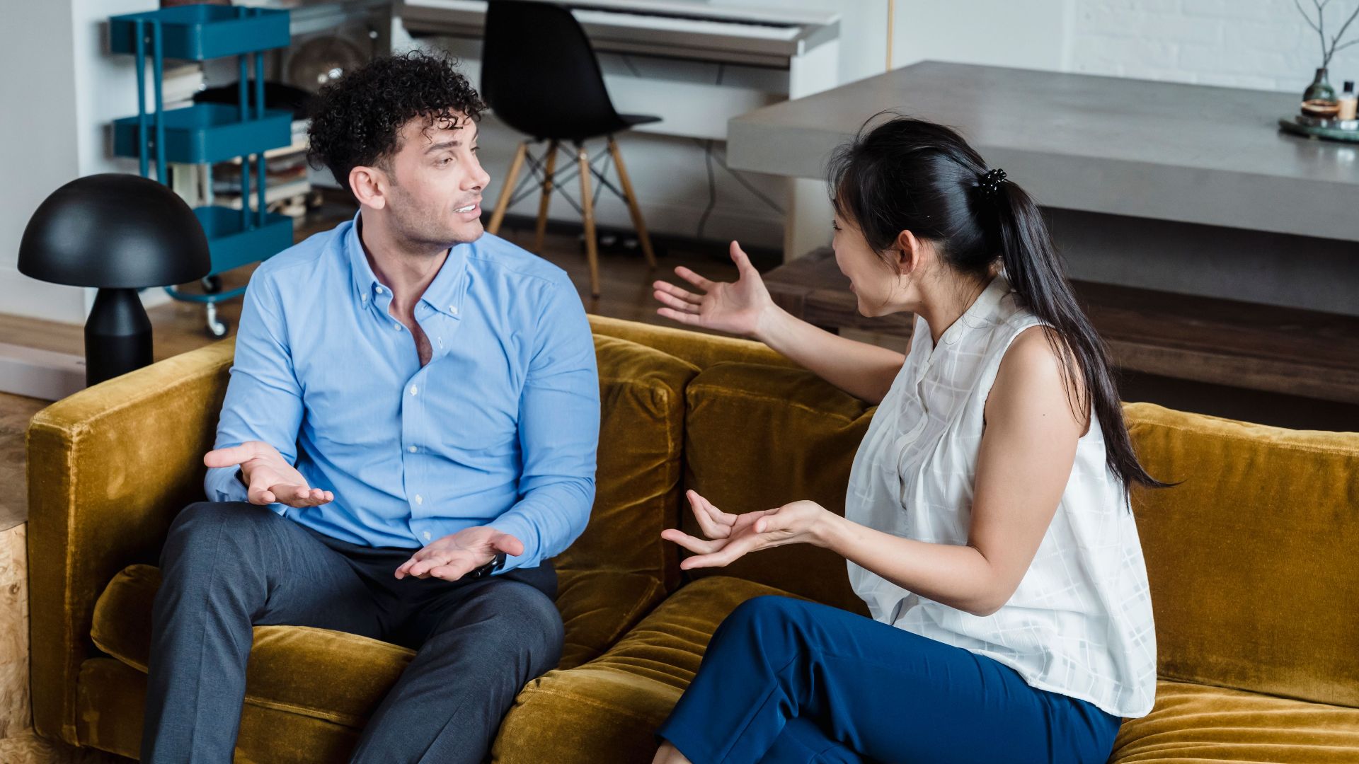 A man and woman engaged in an animated discussion while sitting on a sofa in a modern living room.