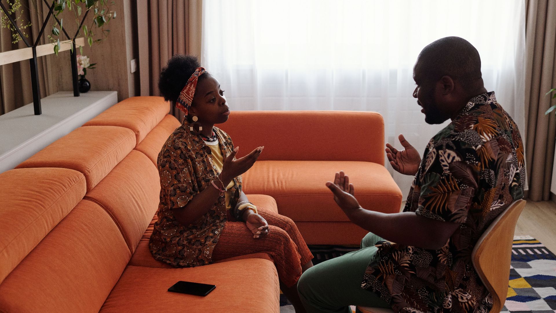 A couple having an emotional discussion on an orange sofa in modern living room.