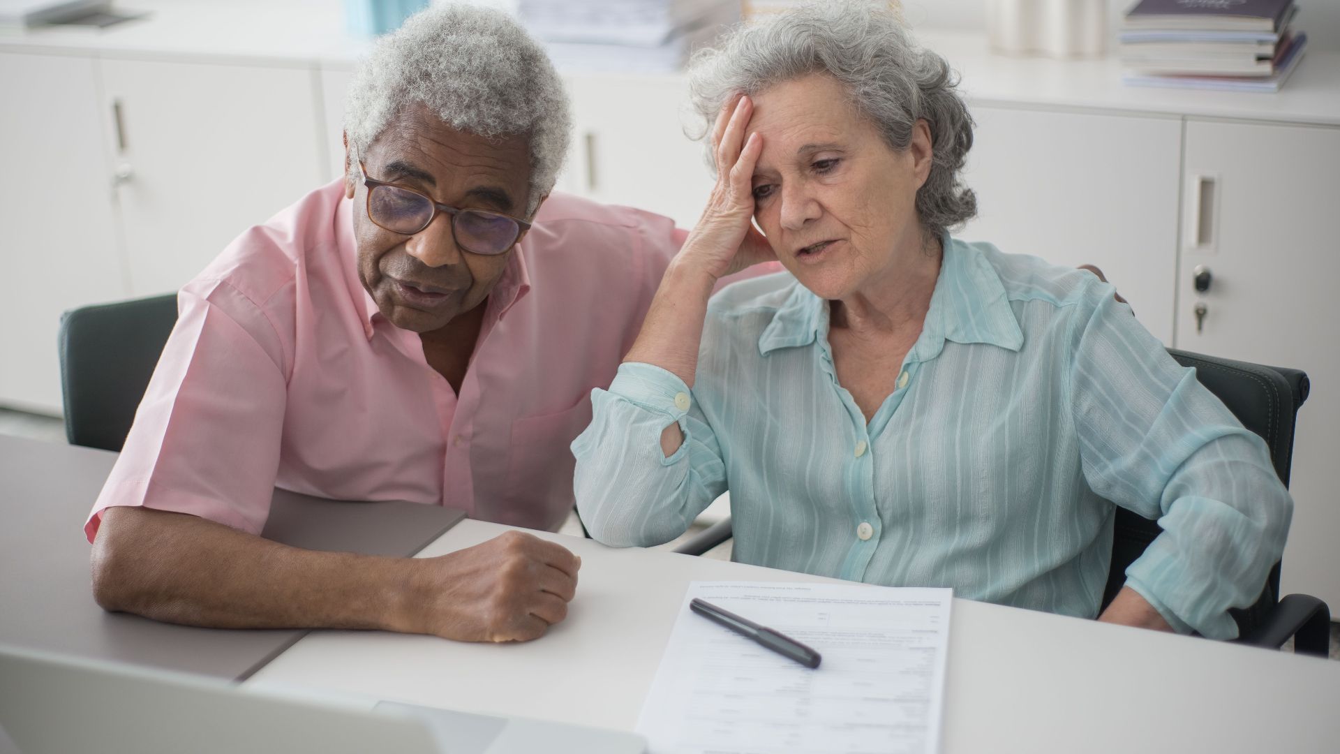 Elderly couple engaged with a laptop, reviewing paperwork at home office desk.