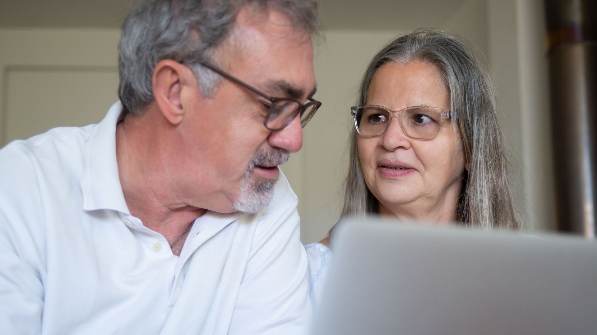 A senior couple engaging with technology at home, discussing content on a laptop.
