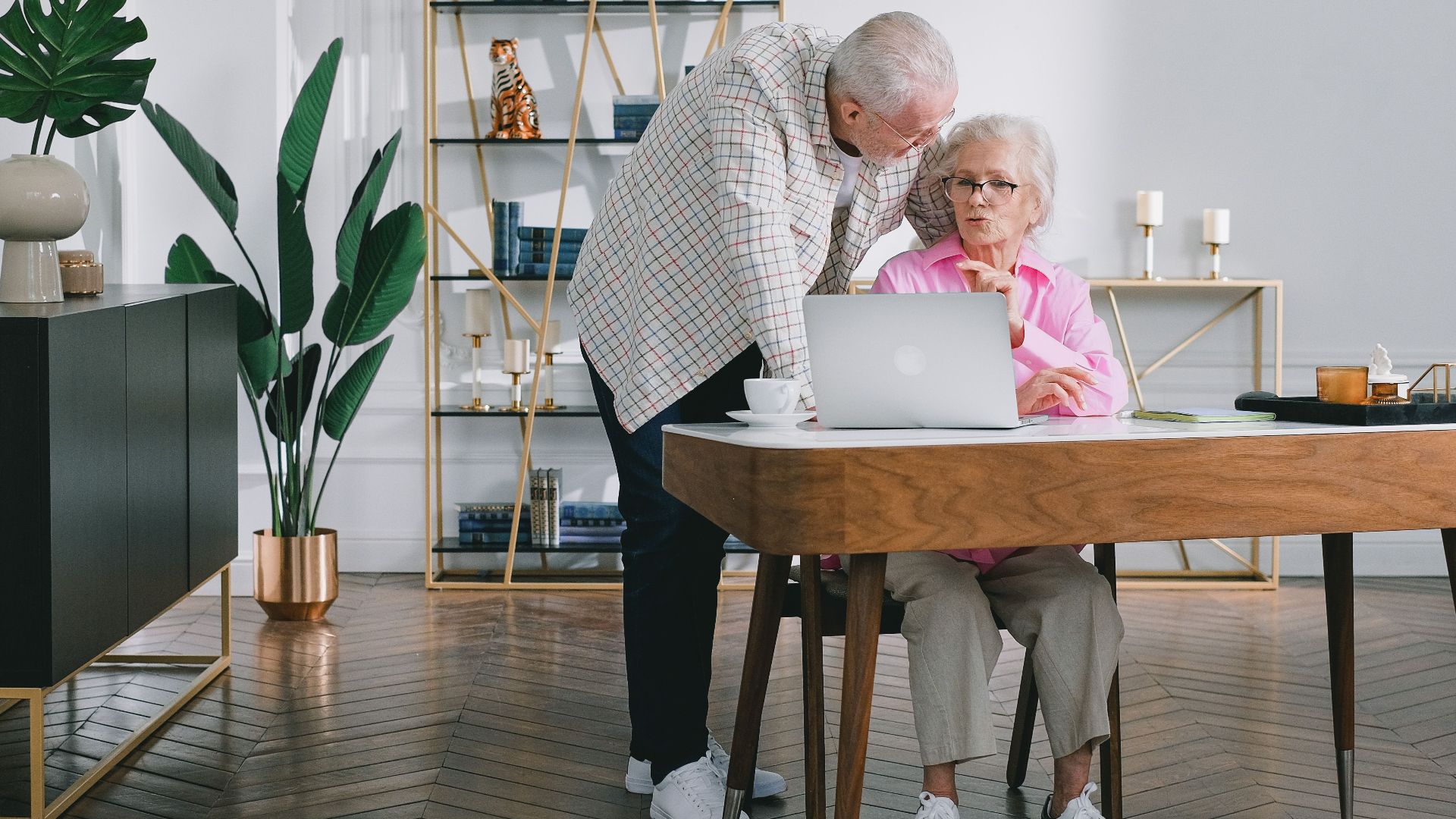 Senior couple using a laptop while discussing something in their modern living room.