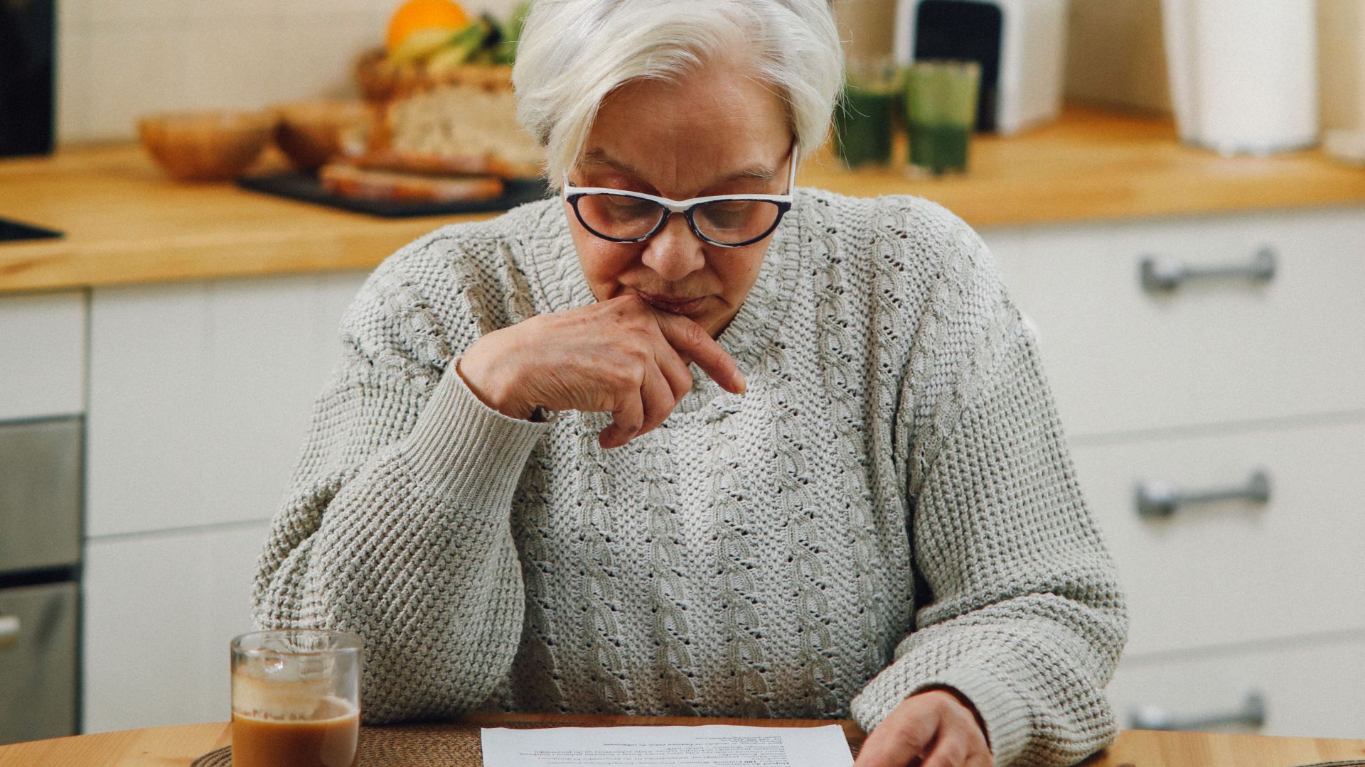 Senior woman reading at a kitchen table, deep in thought.