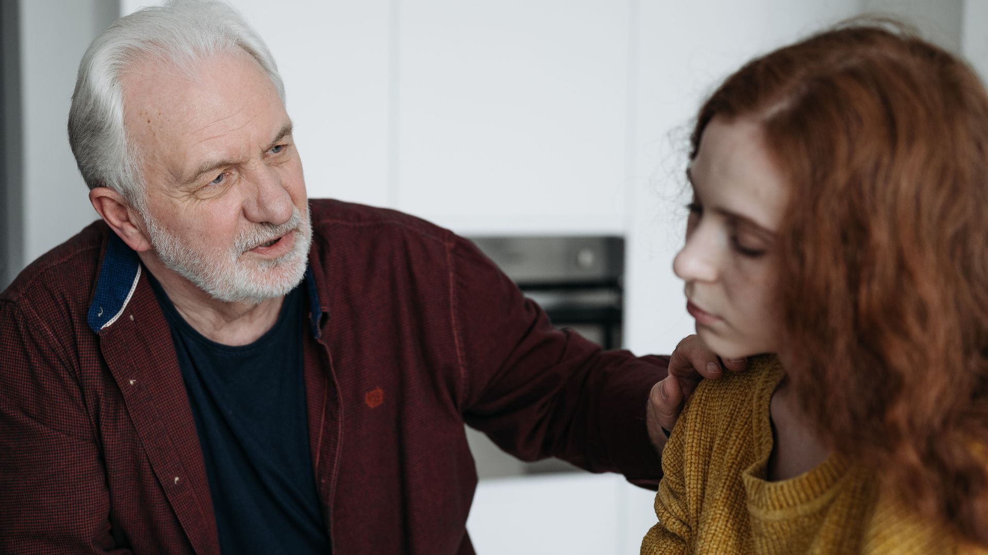 An elderly man consoles a young woman indoors, expressing empathy and understanding.