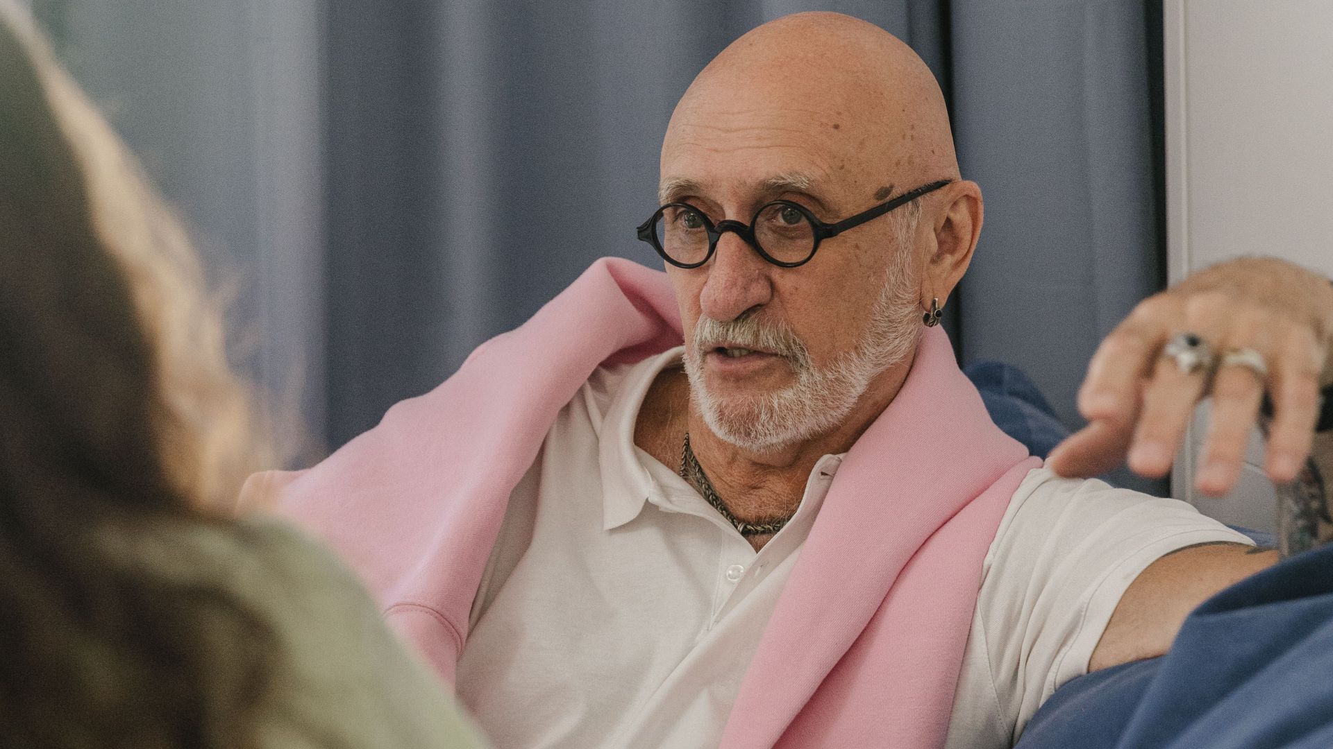 Senior man with glasses and facial hair engaged in conversation on a sofa indoors.