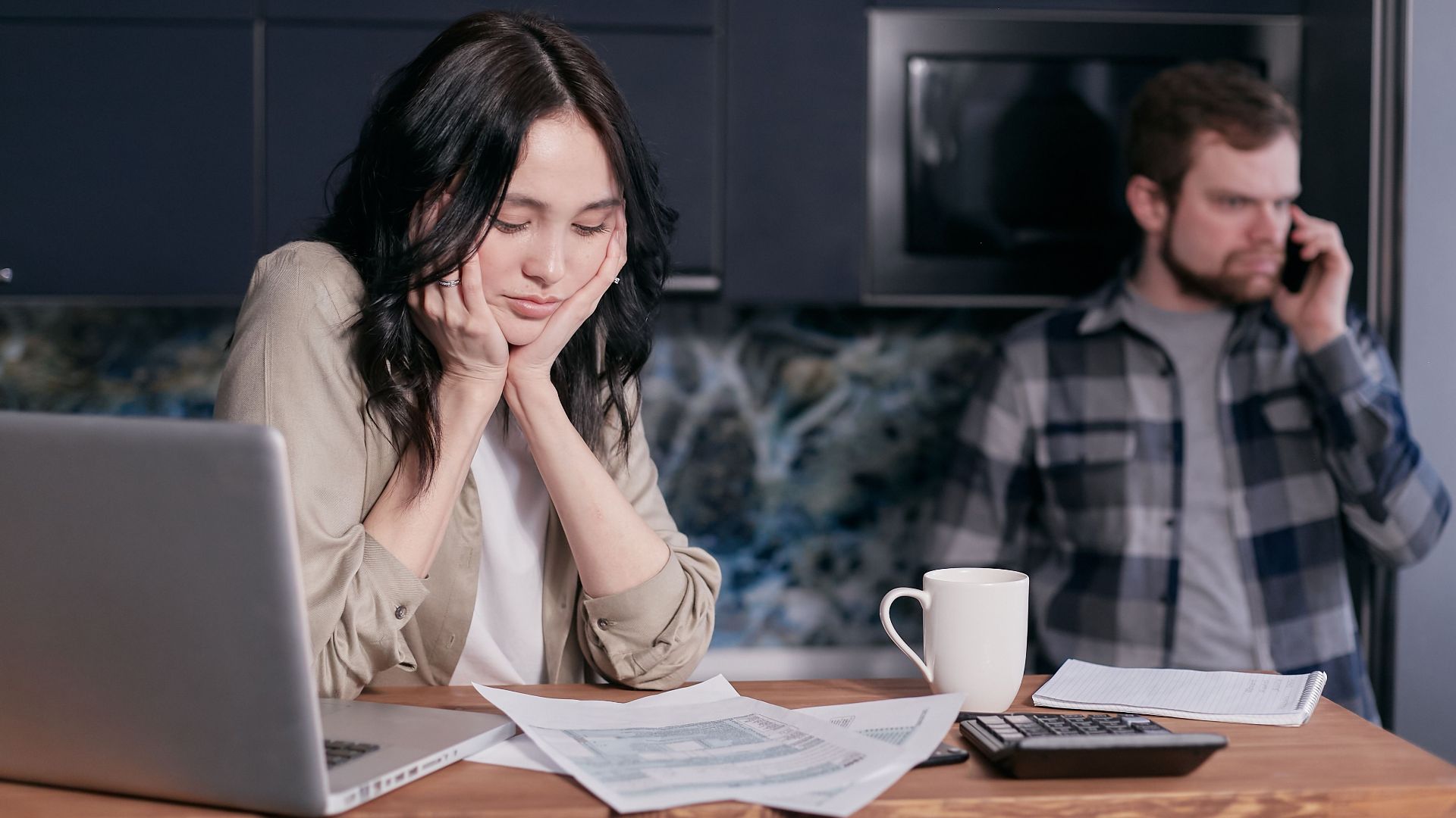 Couple dealing with financial stress at home, surrounded by bills and a laptop.