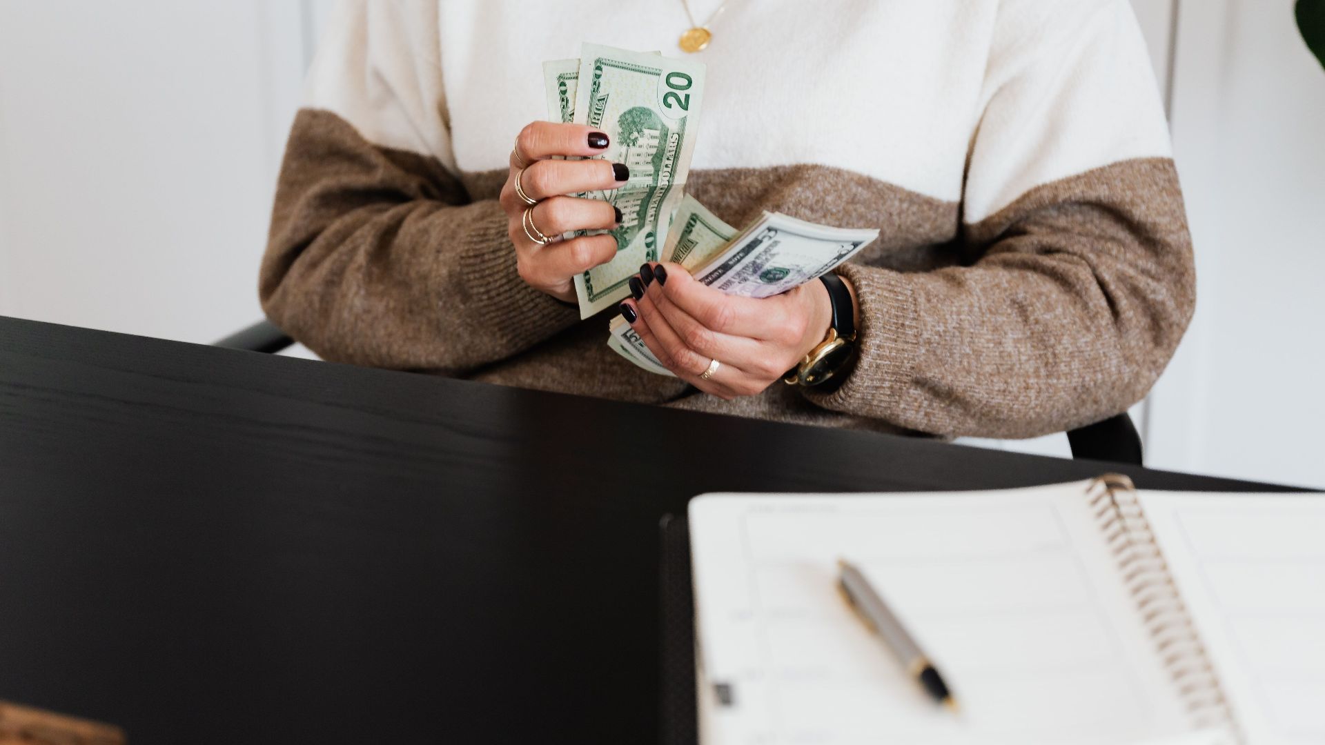 Close-up of an adult counting dollar bills at a desk with a notebook.
