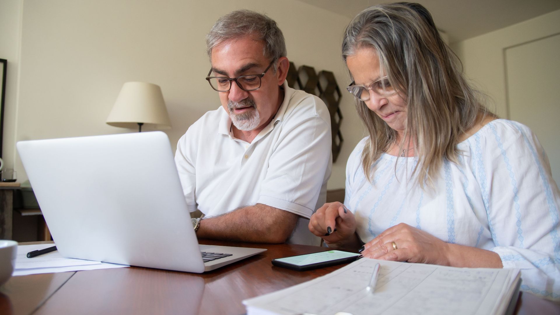 Senior couple working together on documents with laptop and phone at home.