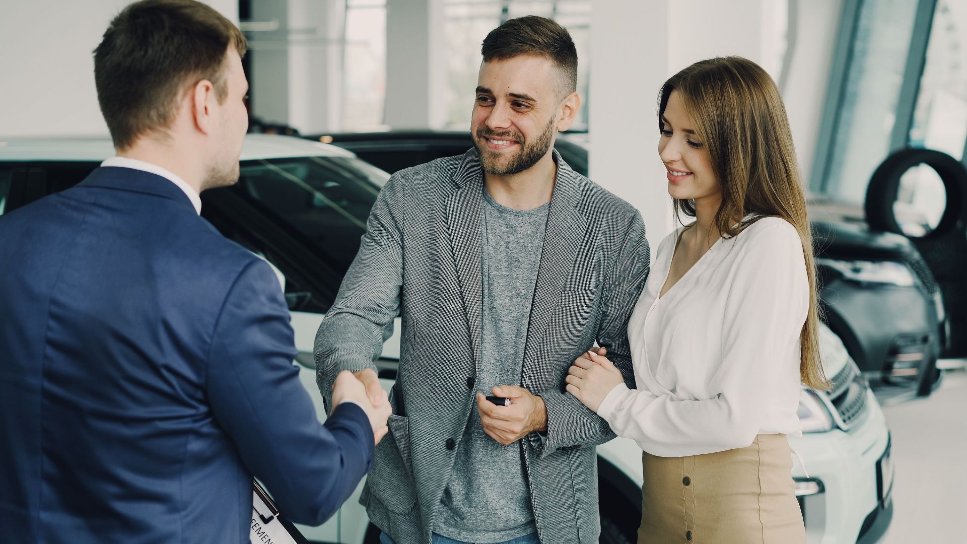 Happy couple finalizing car purchase with salesman in dealership showroom. Bright and welcoming environment.