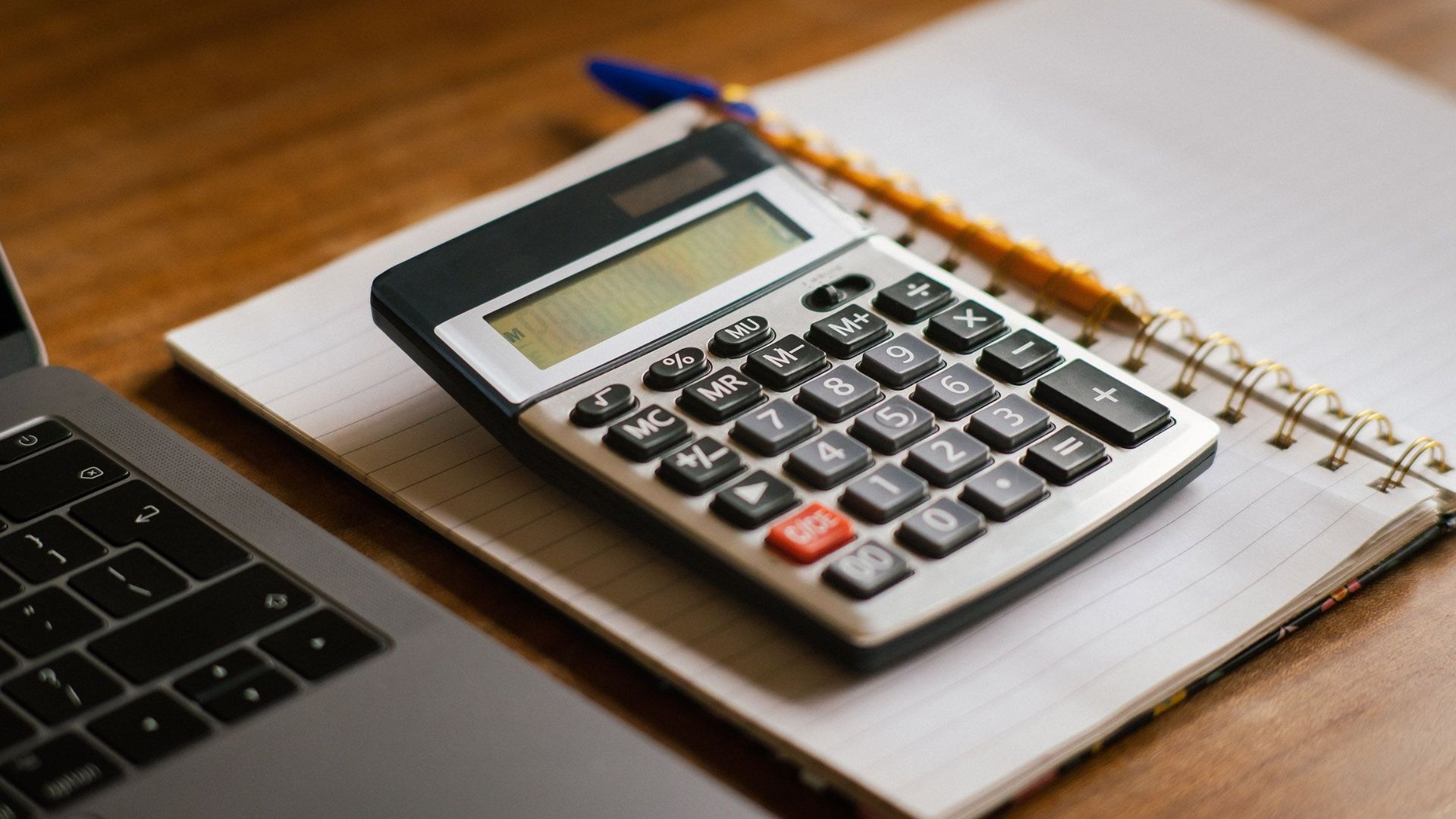 Calculator and open laptop on wooden desk, ideal for financial or accounting tasks.