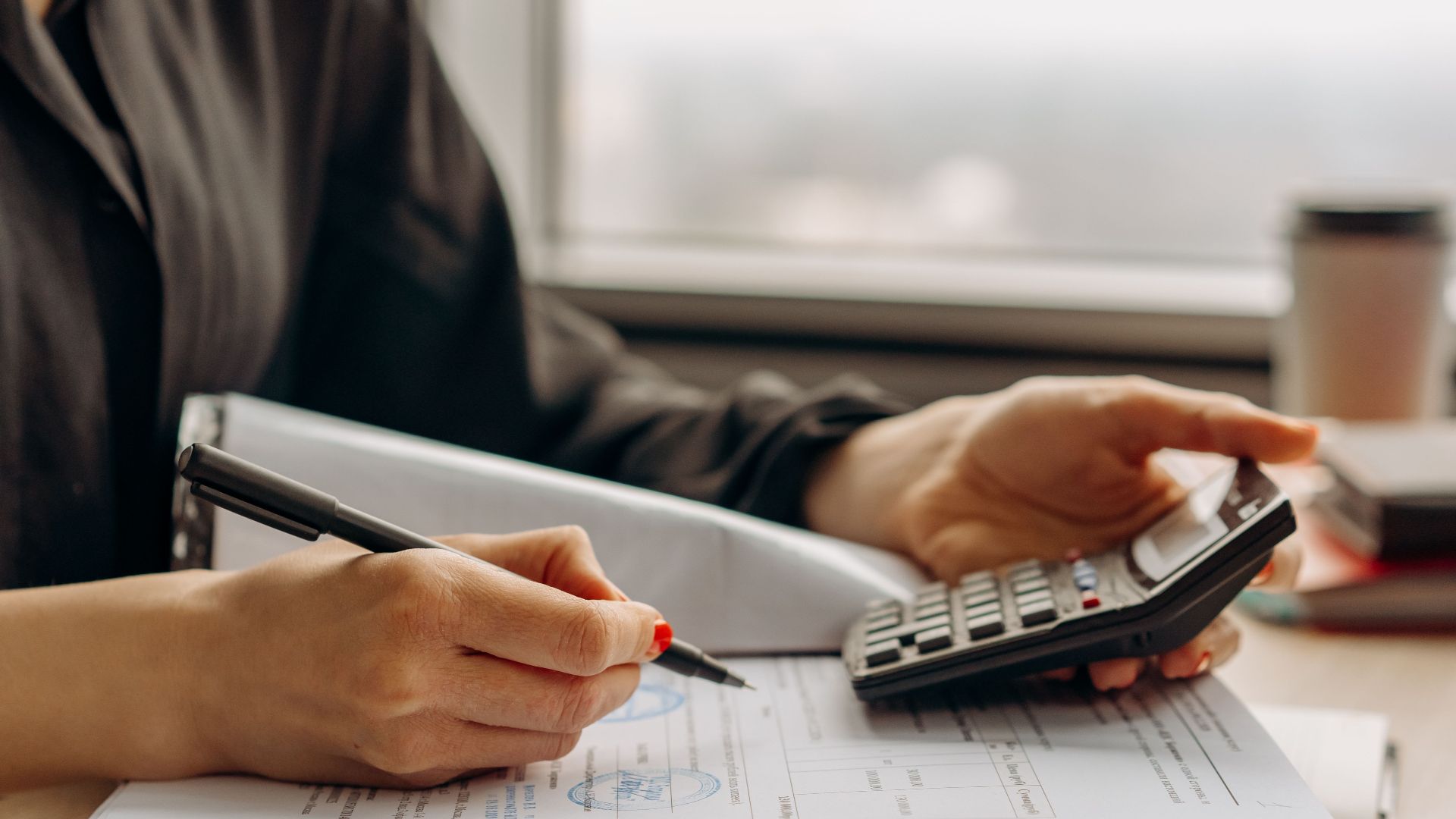 Close-up of person using a calculator with financial documents in an office.