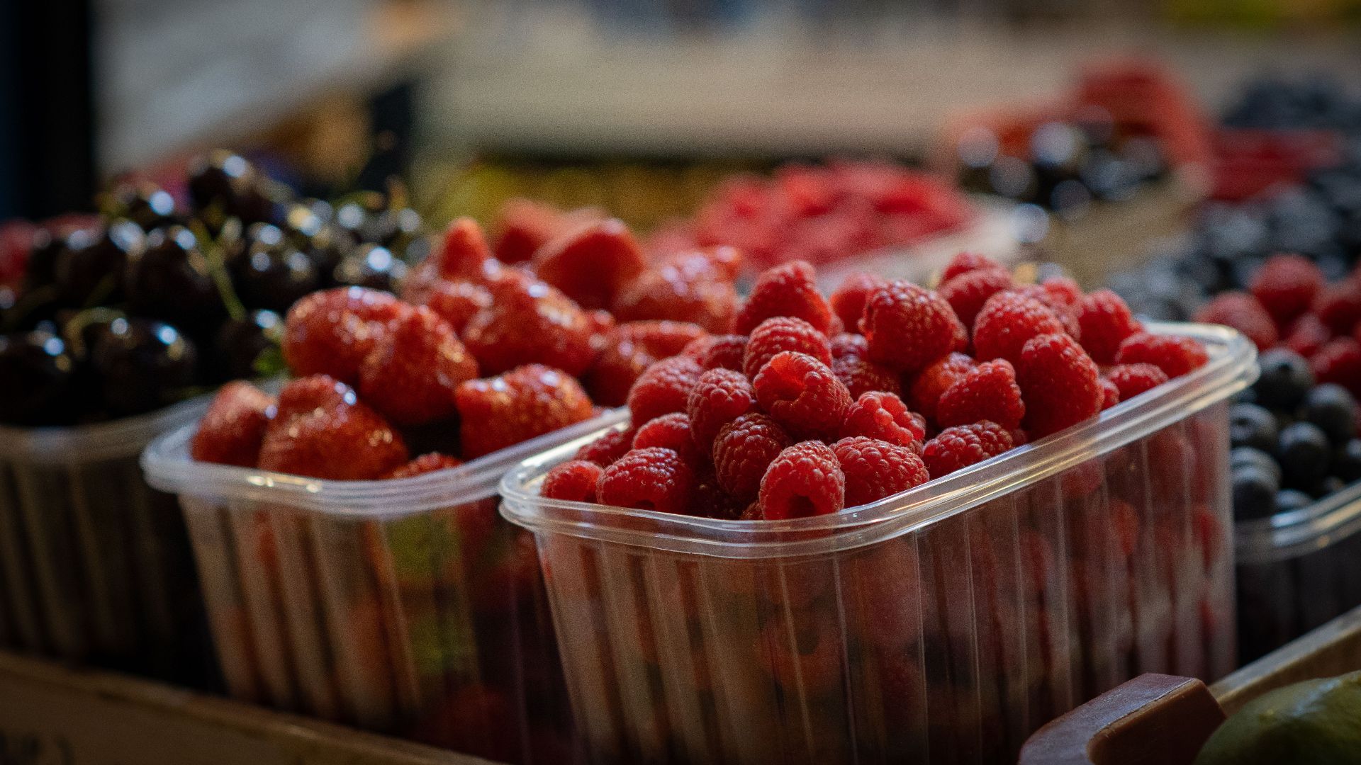 Close-up of fresh raspberries, strawberries, and cherries in plastic containers at a market.