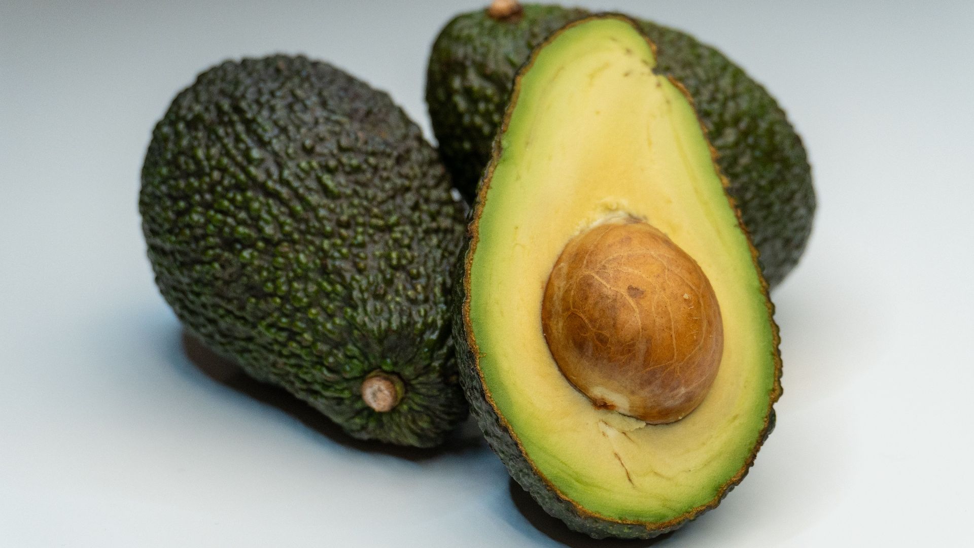 Close-up view of a ripe avocado halved, revealing its seed against a smooth background.