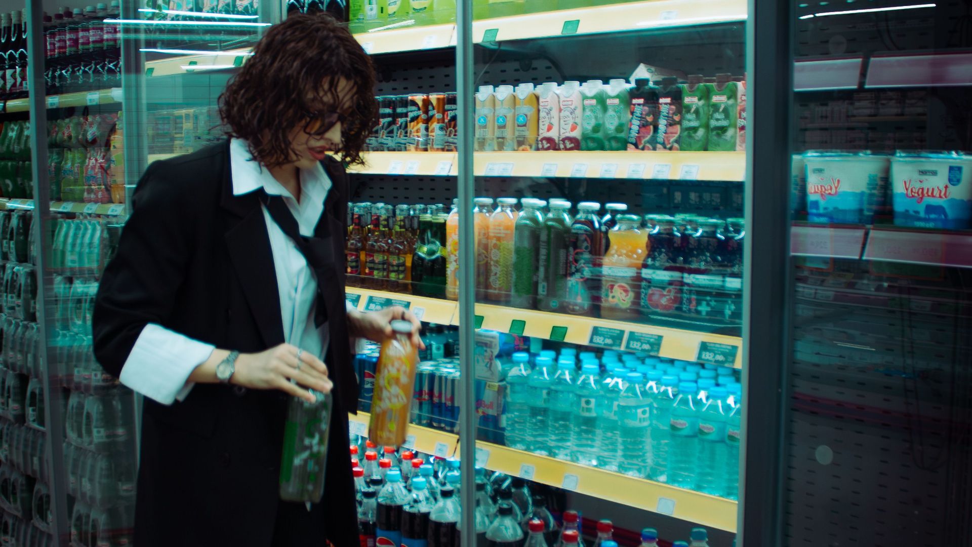 Woman choosing drinks in a grocery store aisle with a shopping basket.