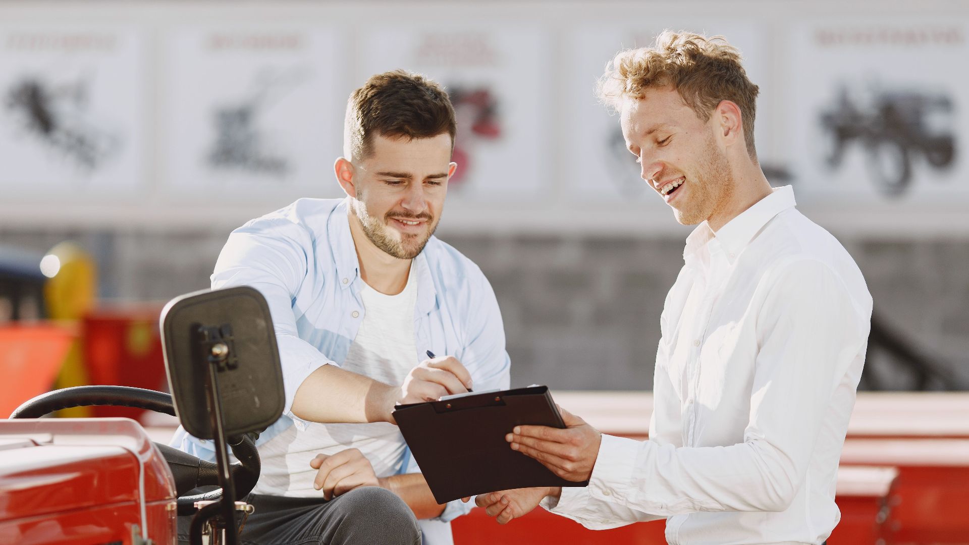 Two men discussing tractor purchase, collaborating outdoors with clipboard.