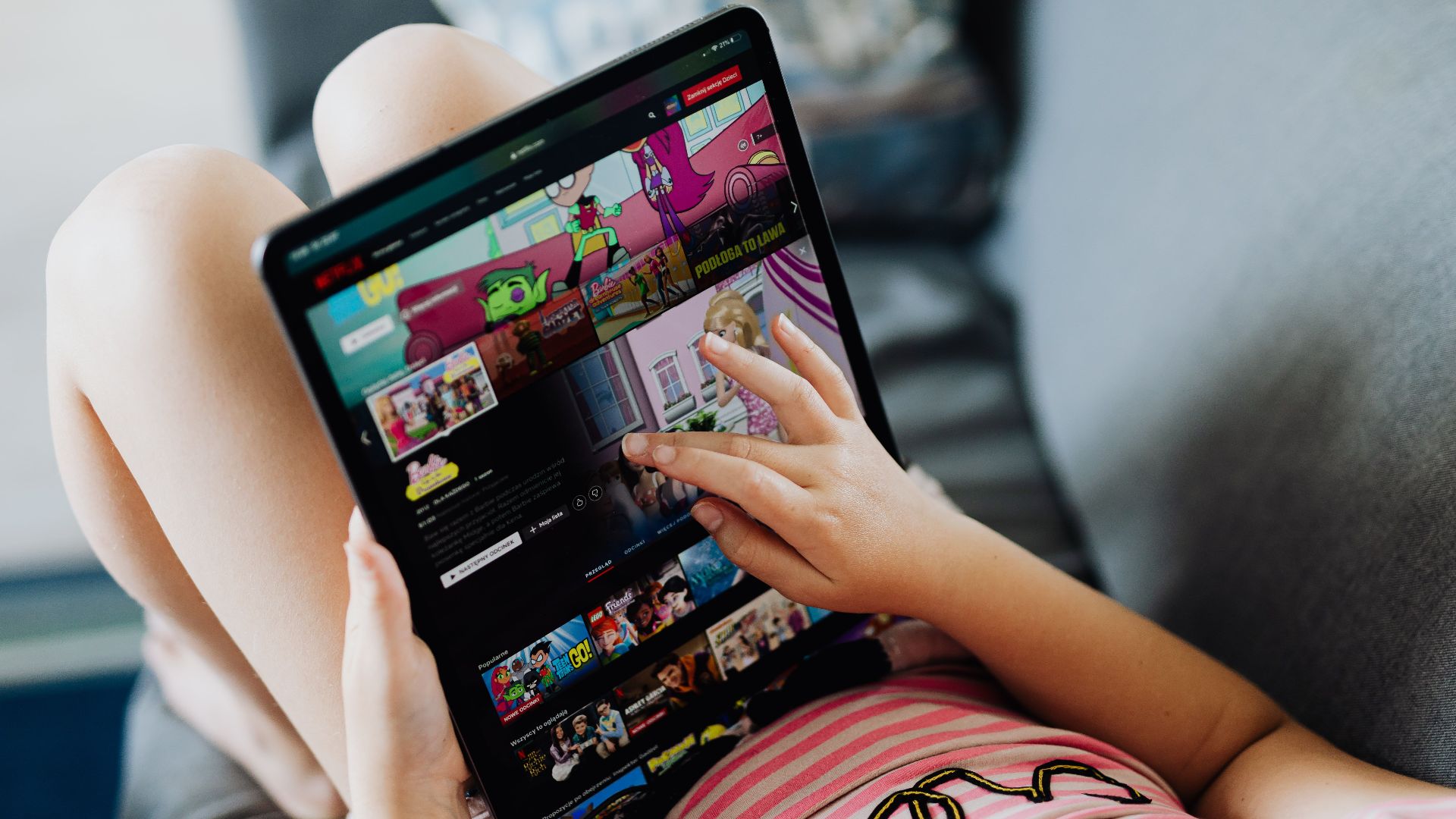 A child using a tablet for streaming cartoons, relaxing on a couch indoors.