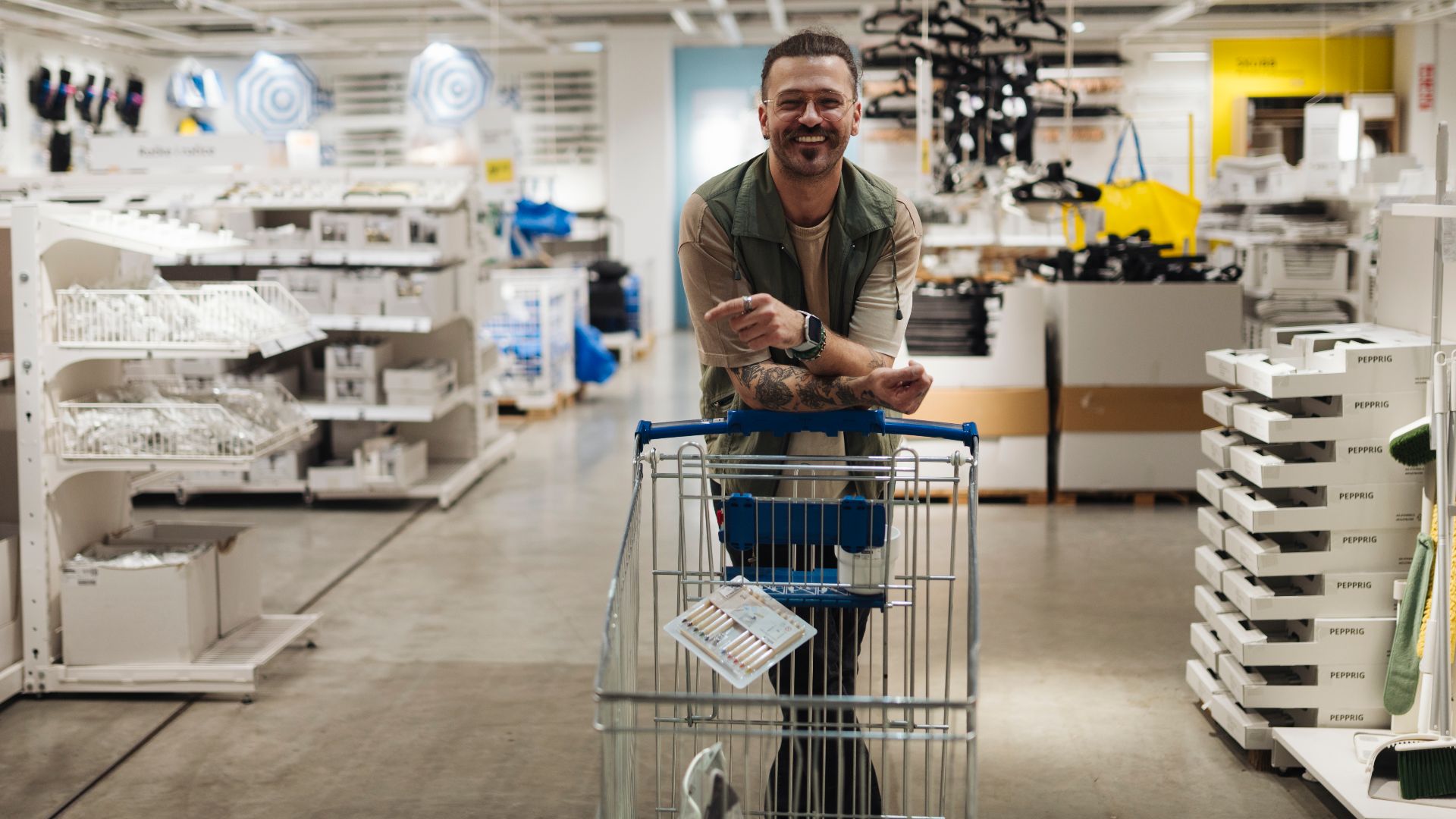 Man smiling while pushing shopping cart down home goods store aisle