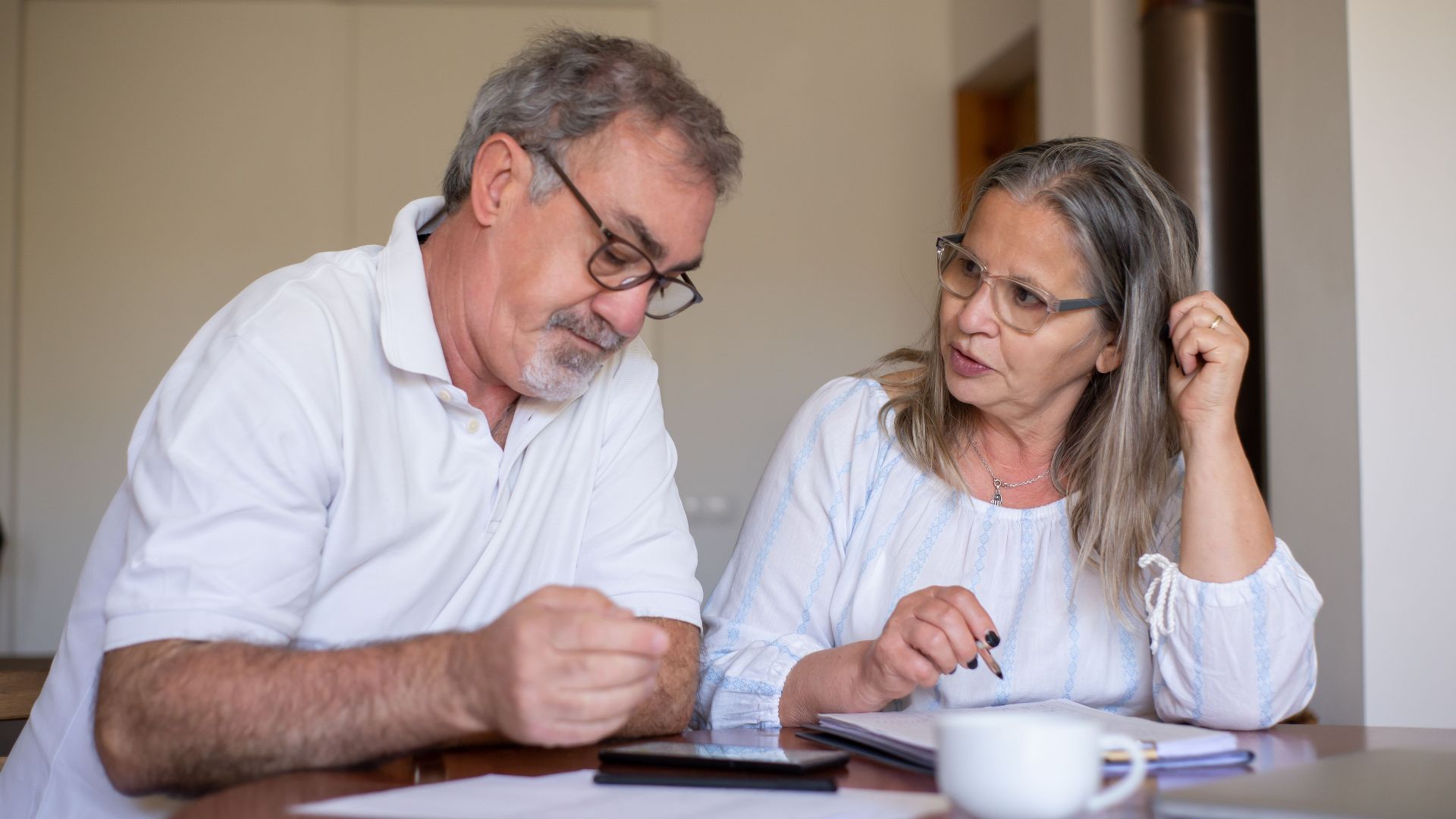 Senior couple reviewing documents and managing finances together at home, showing collaboration and care.
