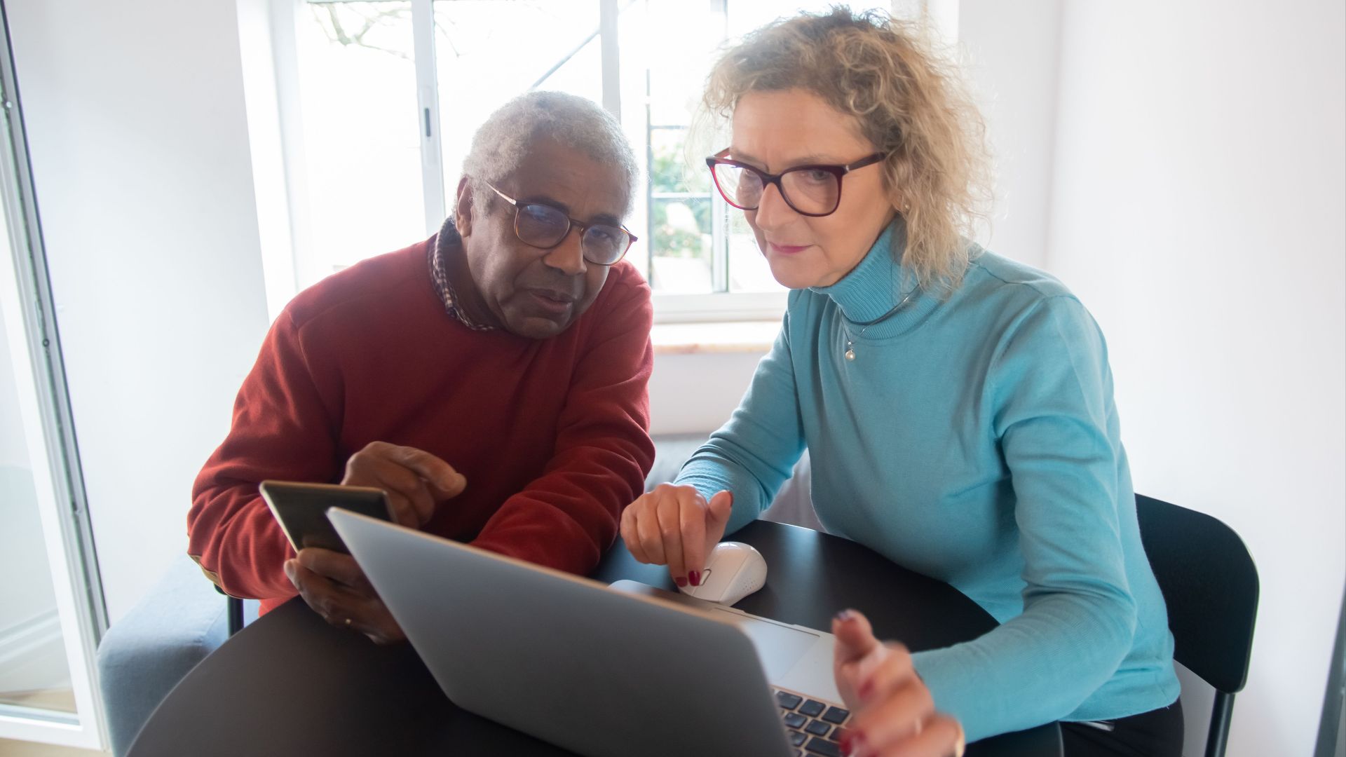 Elderly couple using a laptop in a bright room, focusing on online activities together.