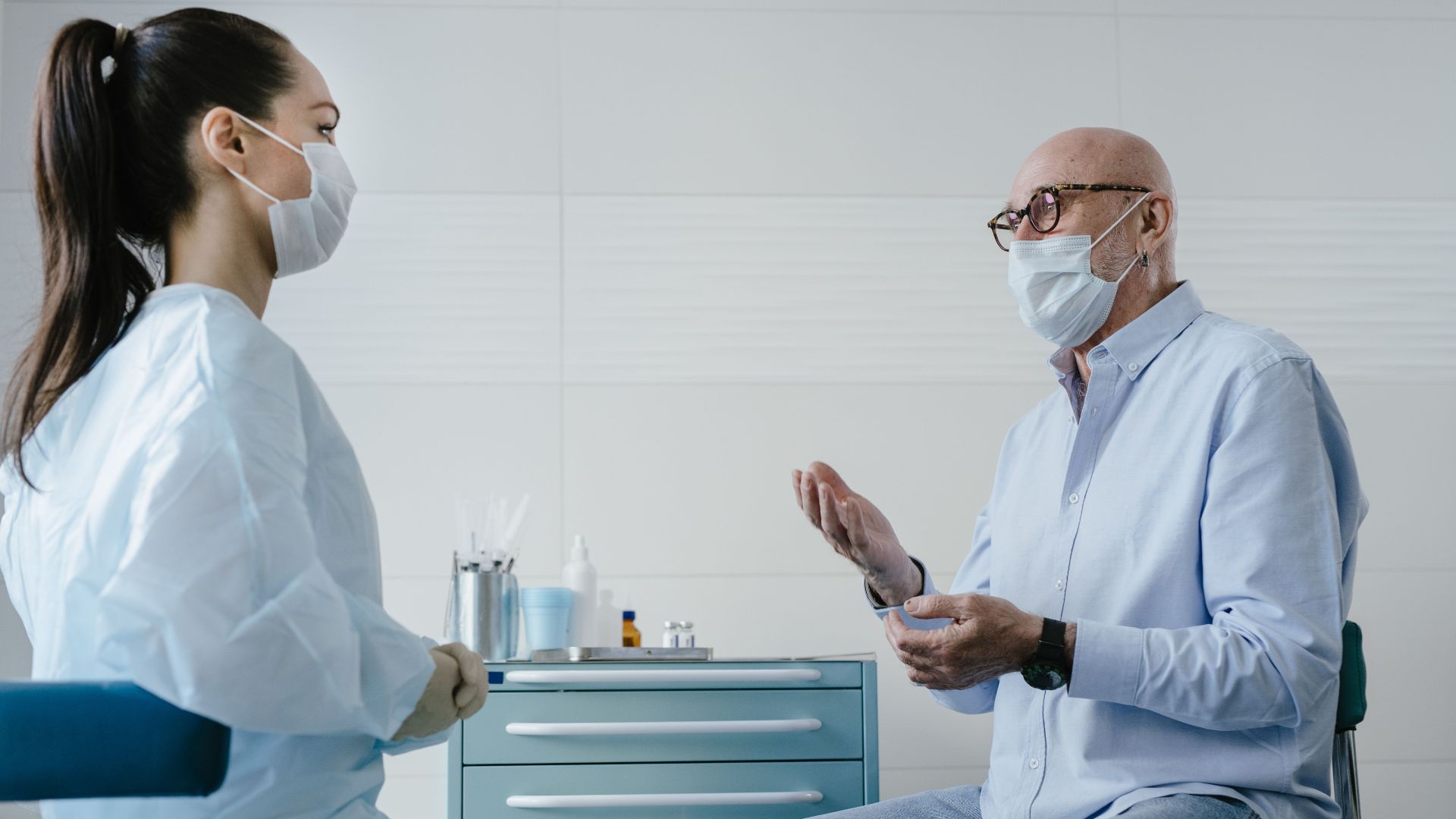 A senior adult patient discusses health concerns with a masked medical professional in a clinic setting.