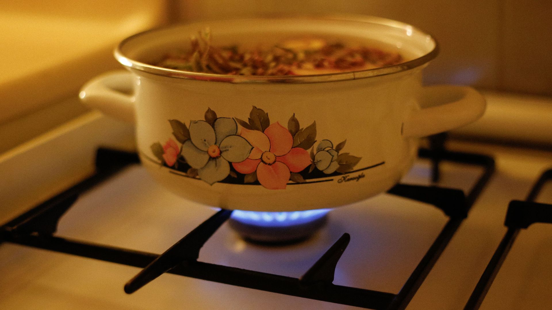 A floral design enamel pot on a gas stove with simmering soup, creating a warm kitchen ambiance.