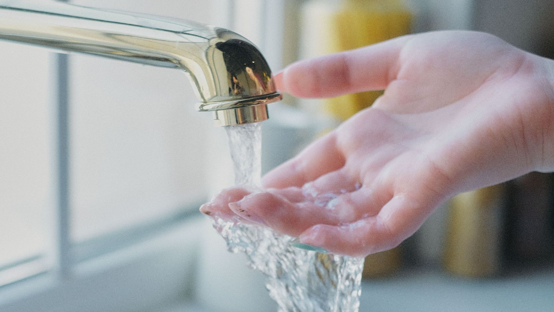 A soft focus image of water flowing over a hand under a kitchen tap, creating a serene ambiance.