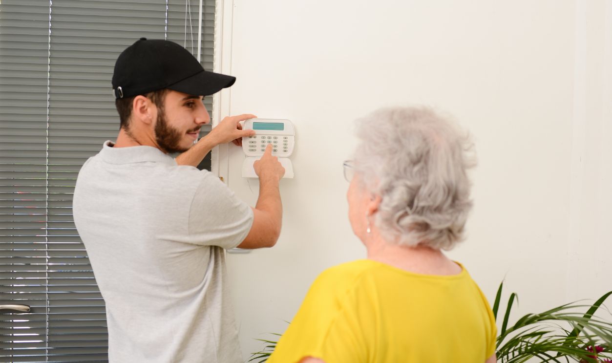 handsome young man installing house security anti burglary camera and siren alarm in a senior woman home