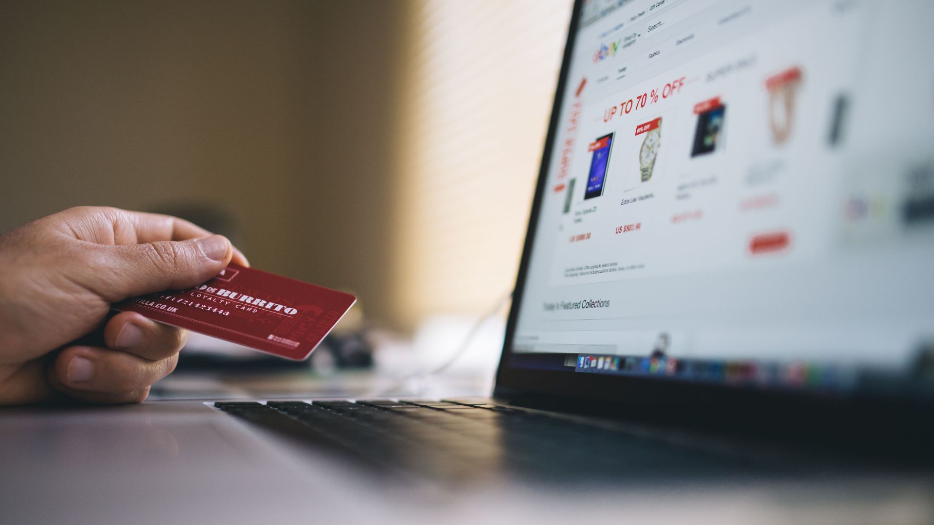 Person holding a credit card while shopping online on a laptop, indicating ecommerce transactions.