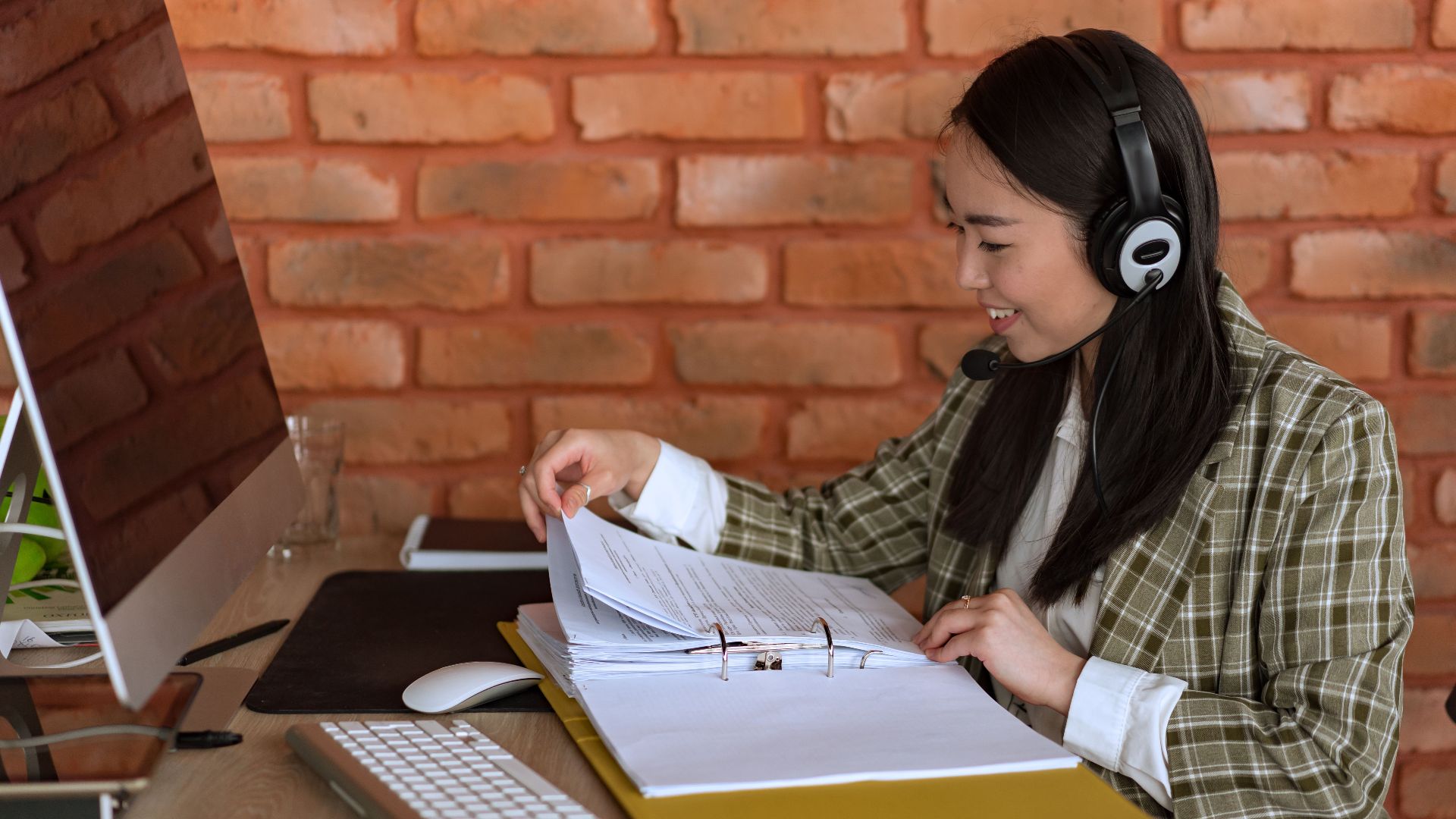 Smiling support agent with a headset and files at her workspace, engaging in a professional environment.