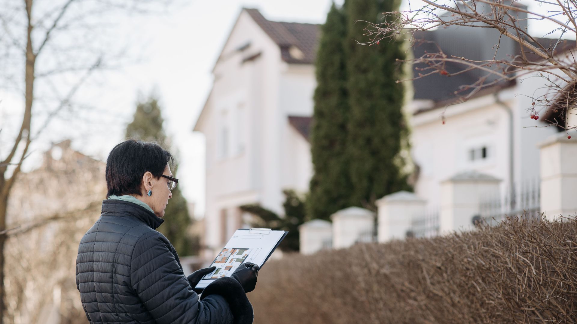 Realtor assessing house with clipboard during winter season outdoors. Ideal image for real estate content.